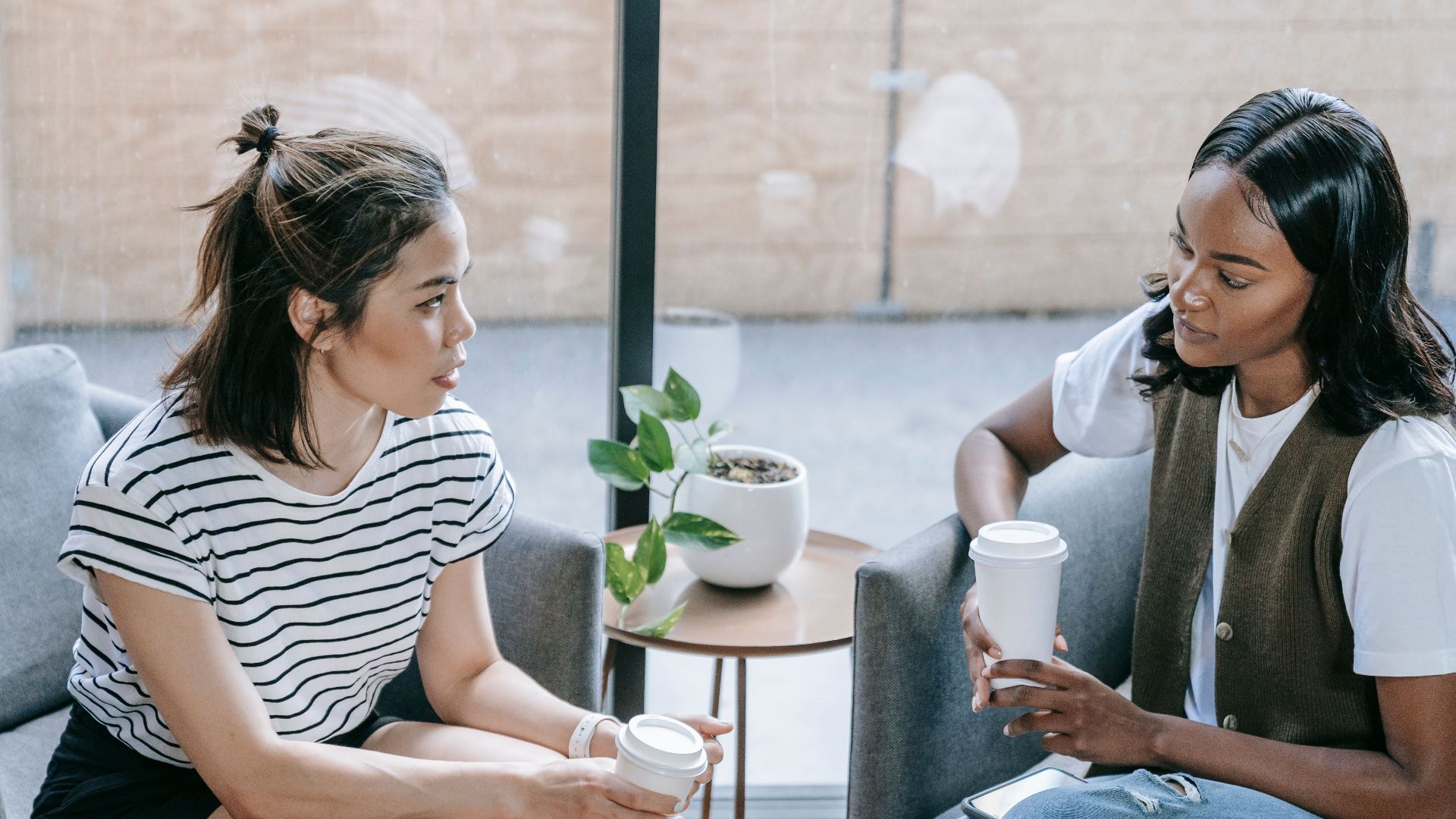 Two young women enjoying coffee and conversation indoors in a cozy setting.