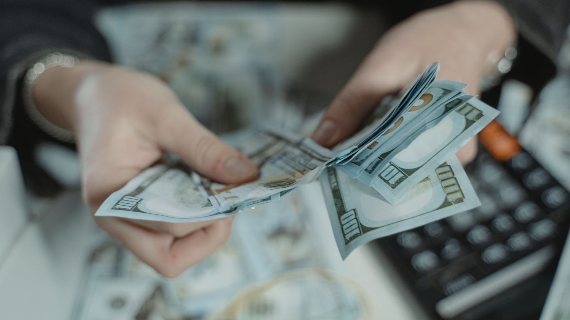 Close-up of hands counting hundred dollar bills with a calculator in the background.