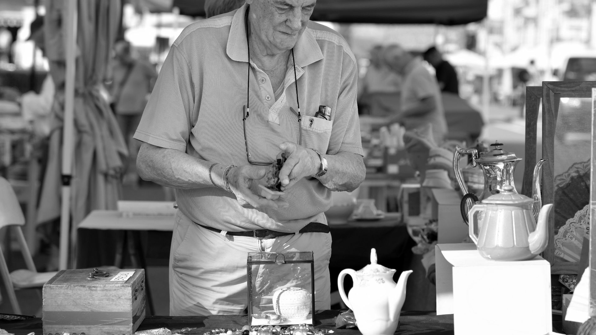 Black and white photo of an elderly man selling antiques at an outdoor market in Italy.