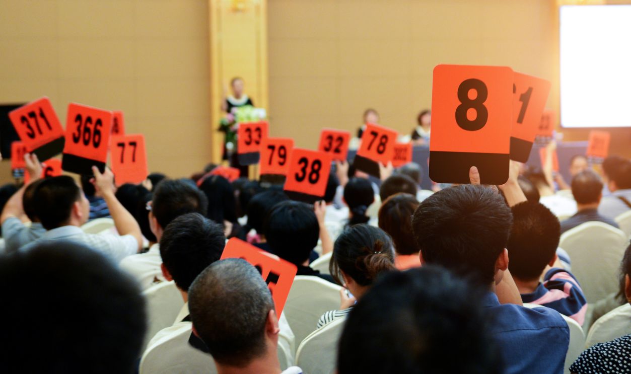 Crowd of bidders holding their numbered bidding paddles at an auction