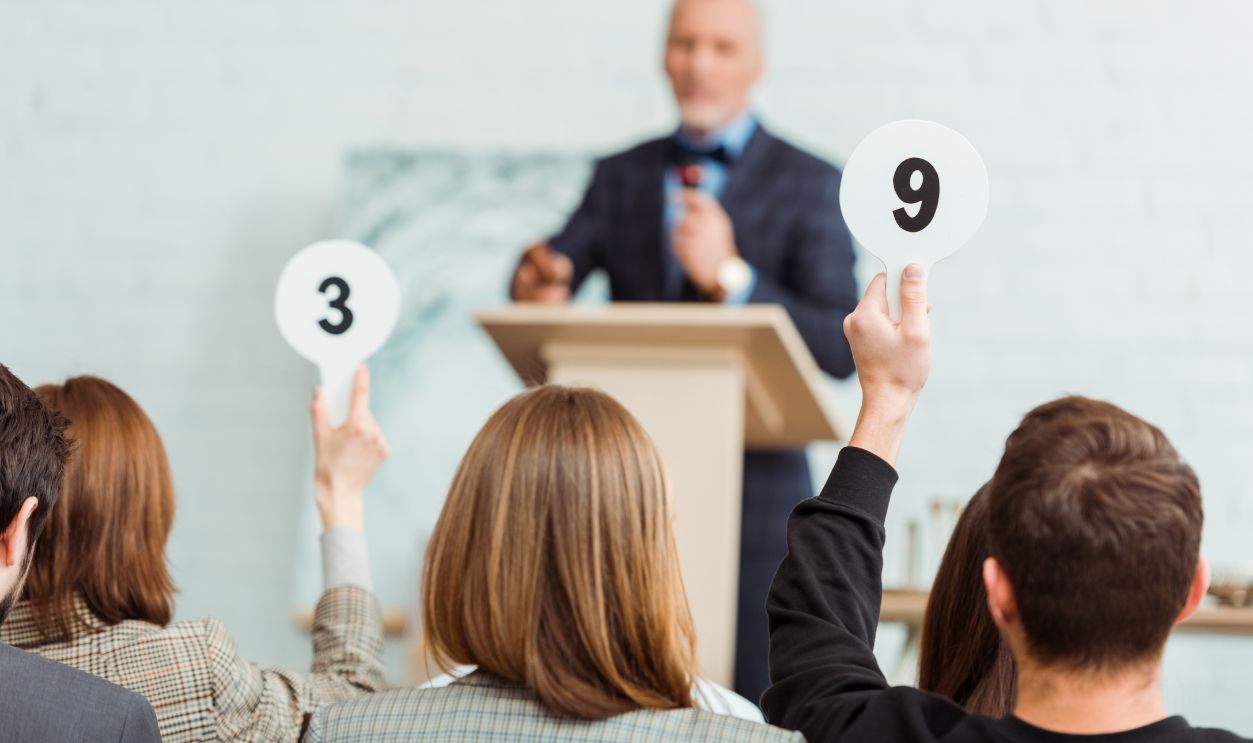 back view of buyers showing auction paddles with numbers nine and three to auctioneer during auction
