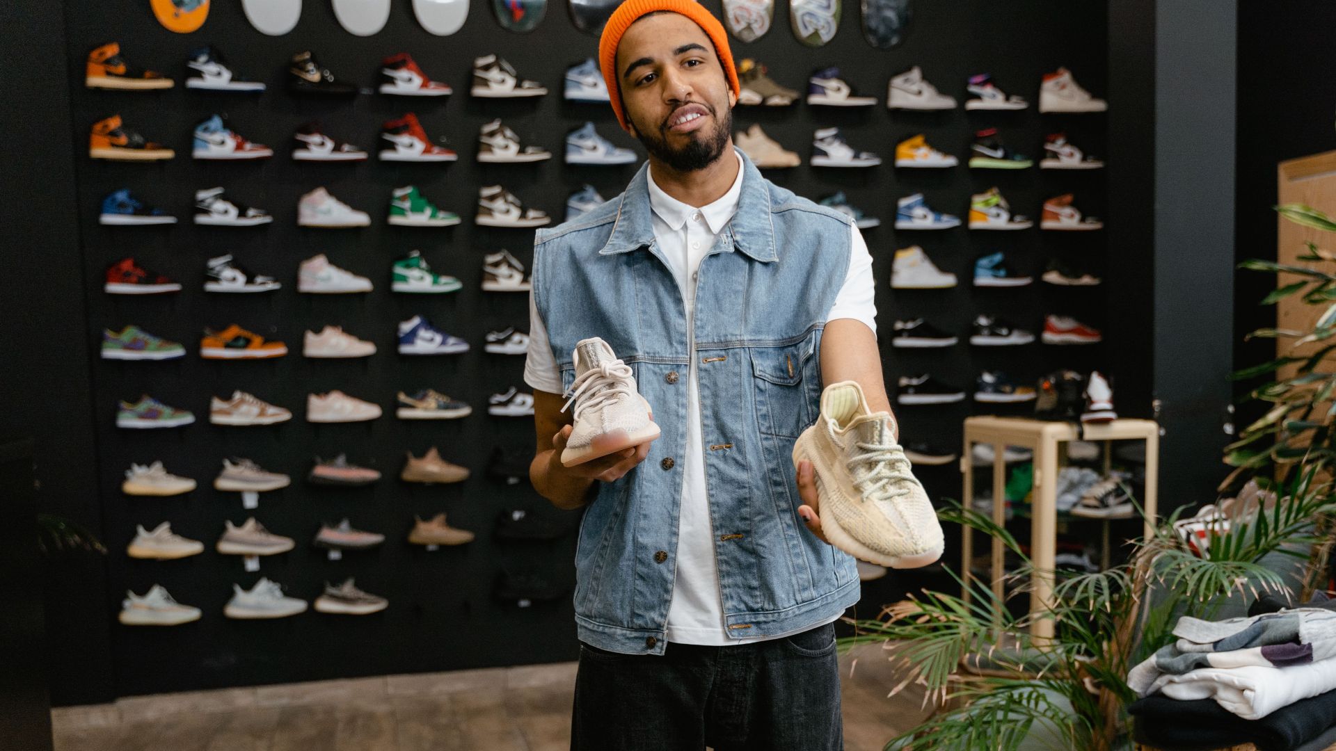 Man showcasing sneakers in a trendy retail fashion store with shoe wall display.
