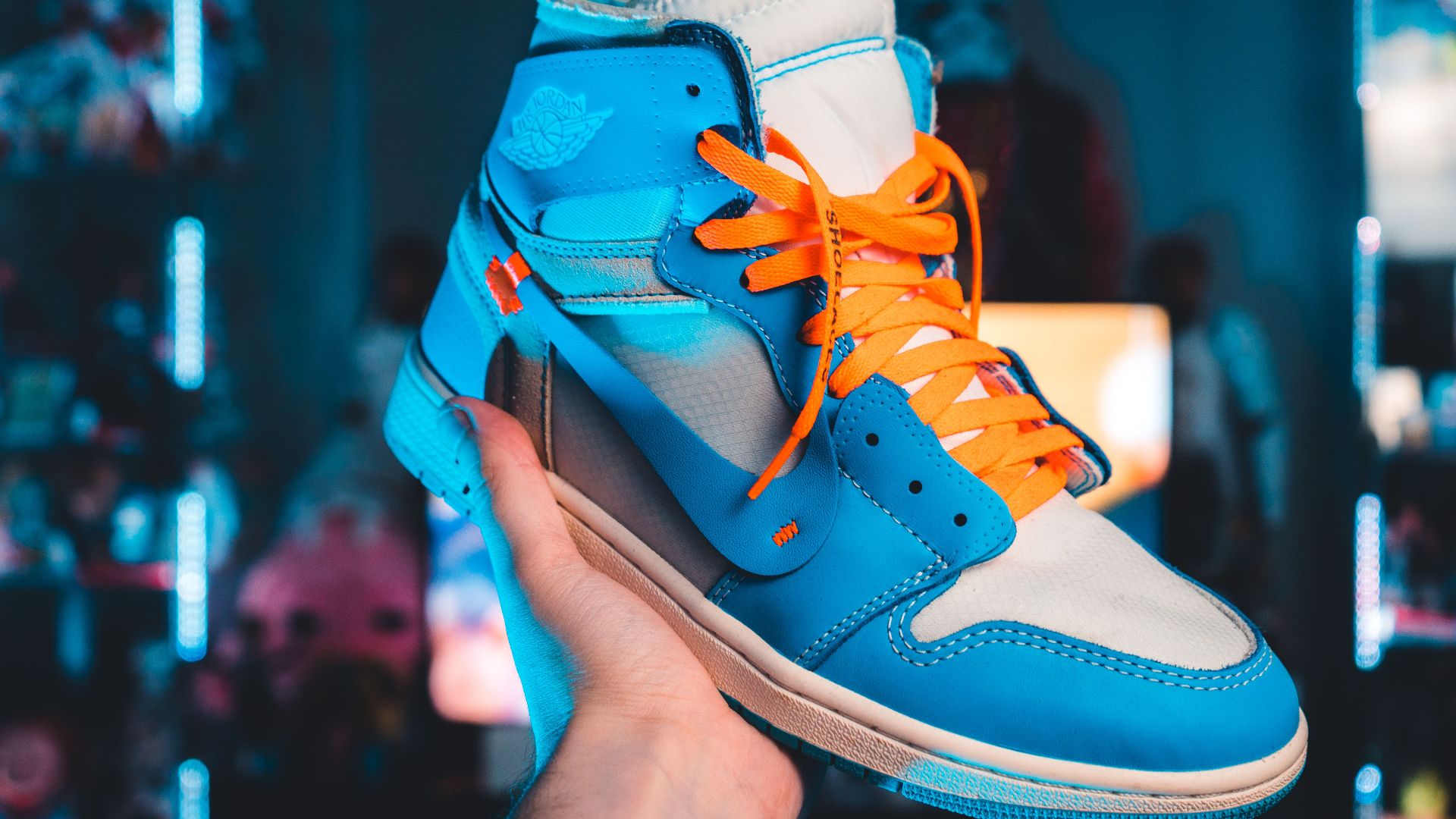 Close-up of a vibrant blue and orange Air Jordan 1 sneaker held in an illuminated setting.