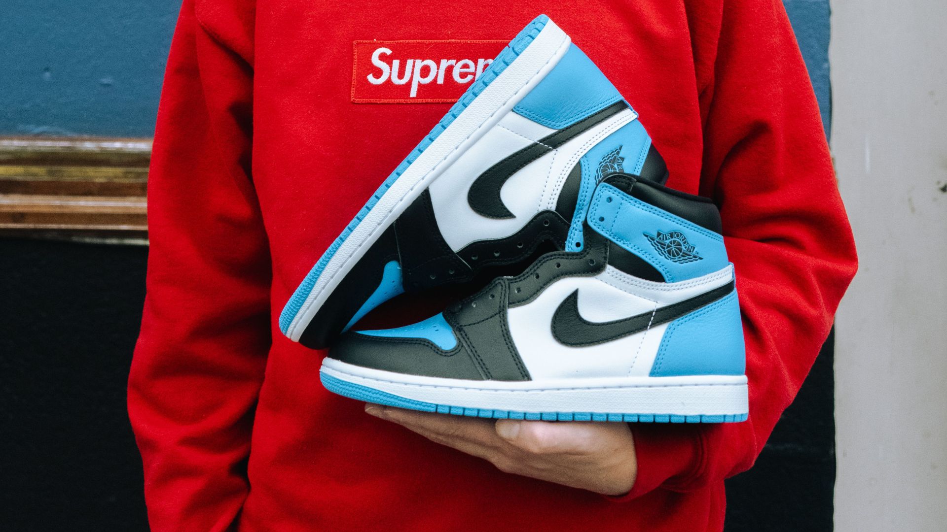 Man in red sweater holding Air Jordan 1 sneakers, showcasing streetwear fashion.