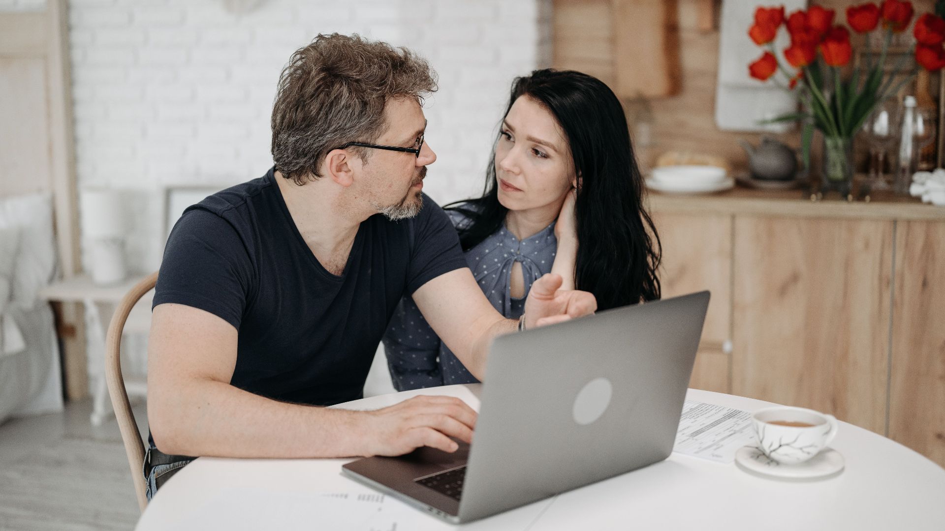 A couple engaged in discussion while using a laptop at a cozy home setting.