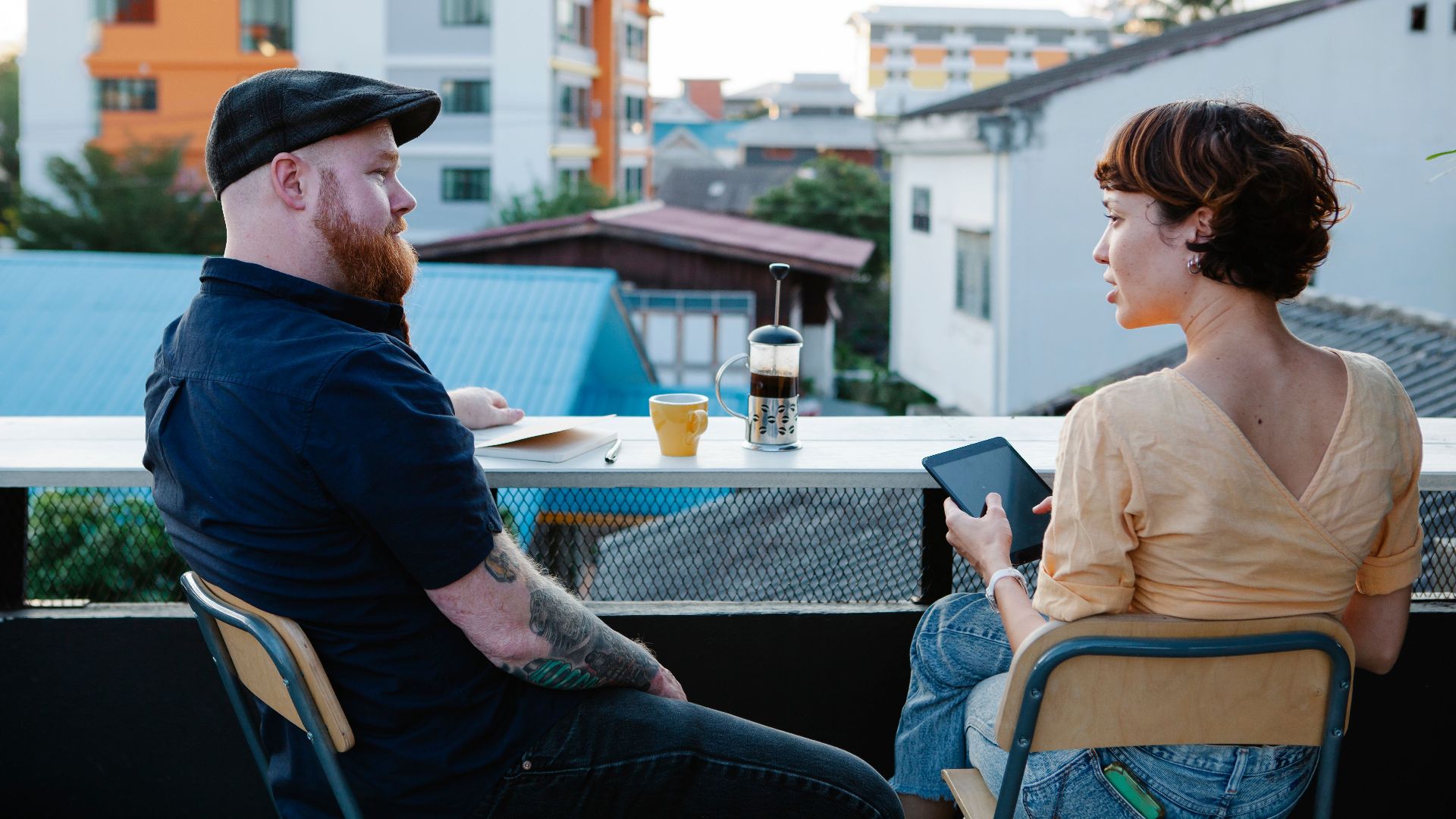 Back view of young woman with tablet and stylish man resting with cup of coffee in terrace in daytime