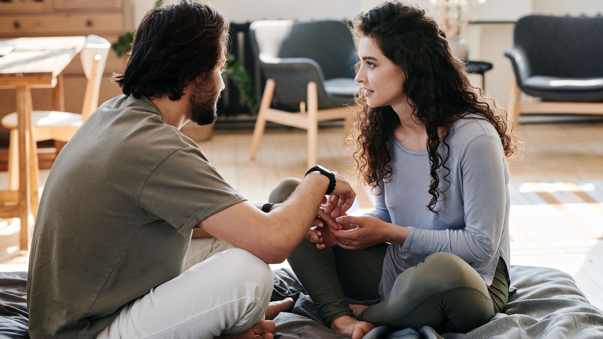 A couple sitting closely on a bed, engaged in a thoughtful discussion in a cozy home setting.