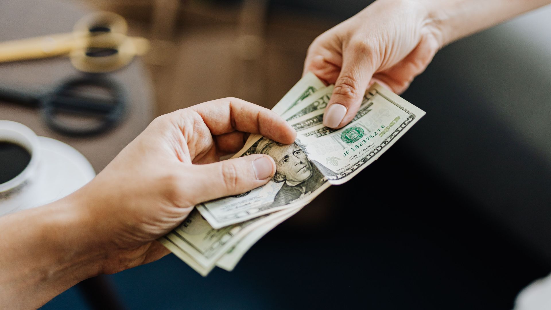 A close-up image of hands exchanging US dollar bills, symbolizing financial transaction or payment.
