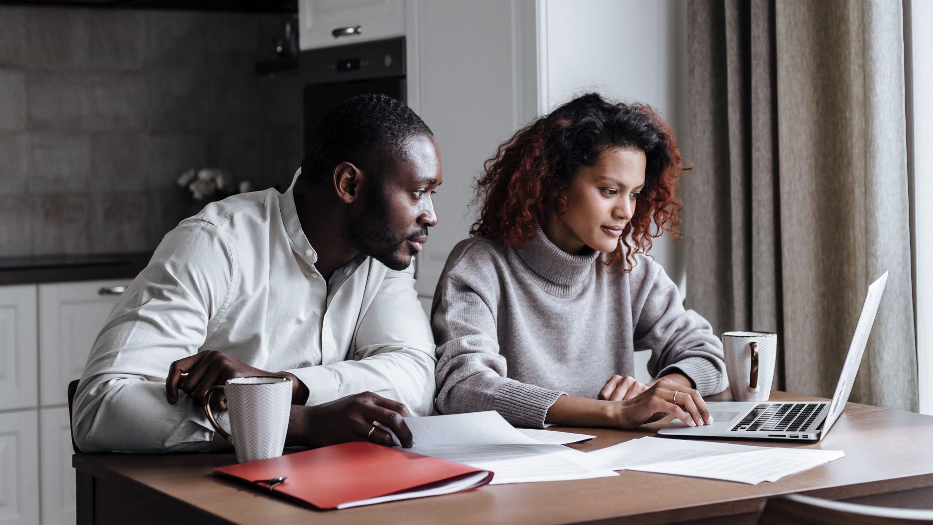 A diverse couple working together on a laptop in a modern kitchen setting, displaying teamwork and collaboration.