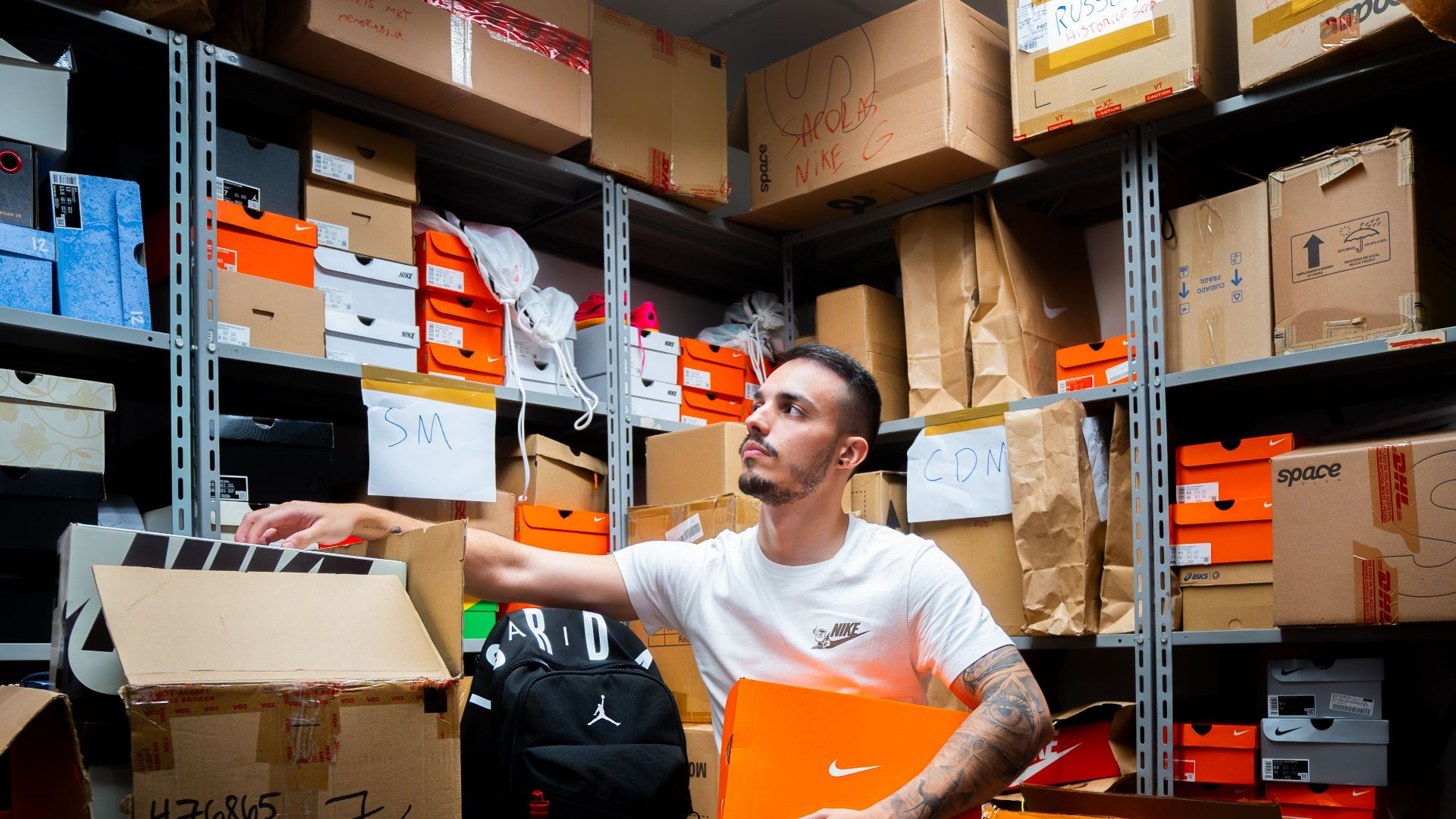 A man organizing a shoe inventory with various branded boxes in a warehouse setting.