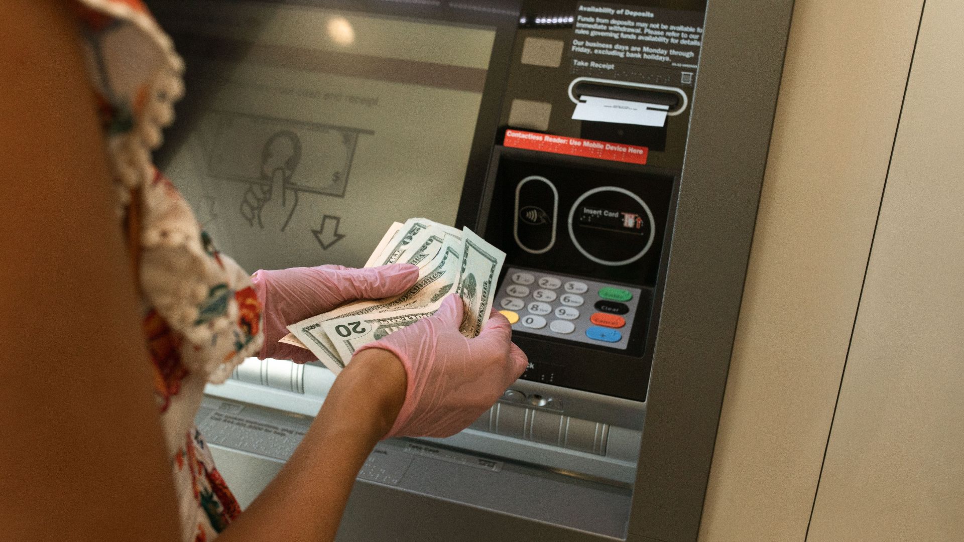 A person wearing gloves withdraws cash from an ATM, ensuring hygiene.