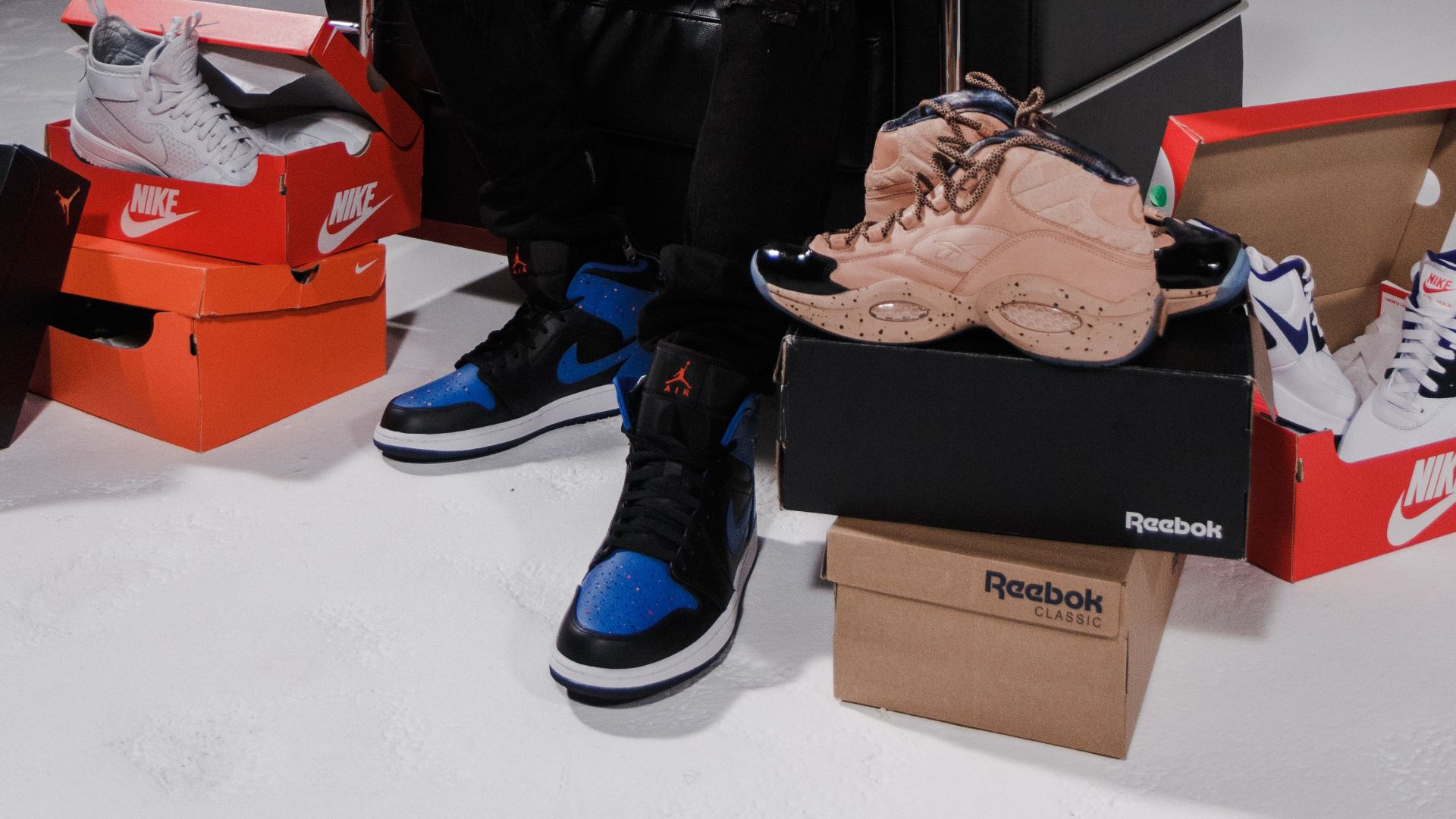 Fashionable man posing with a collection of branded shoes in a studio.