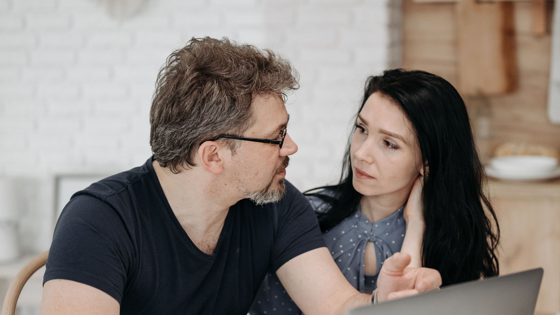 A couple engaged in discussion while using a laptop at a cozy home setting.