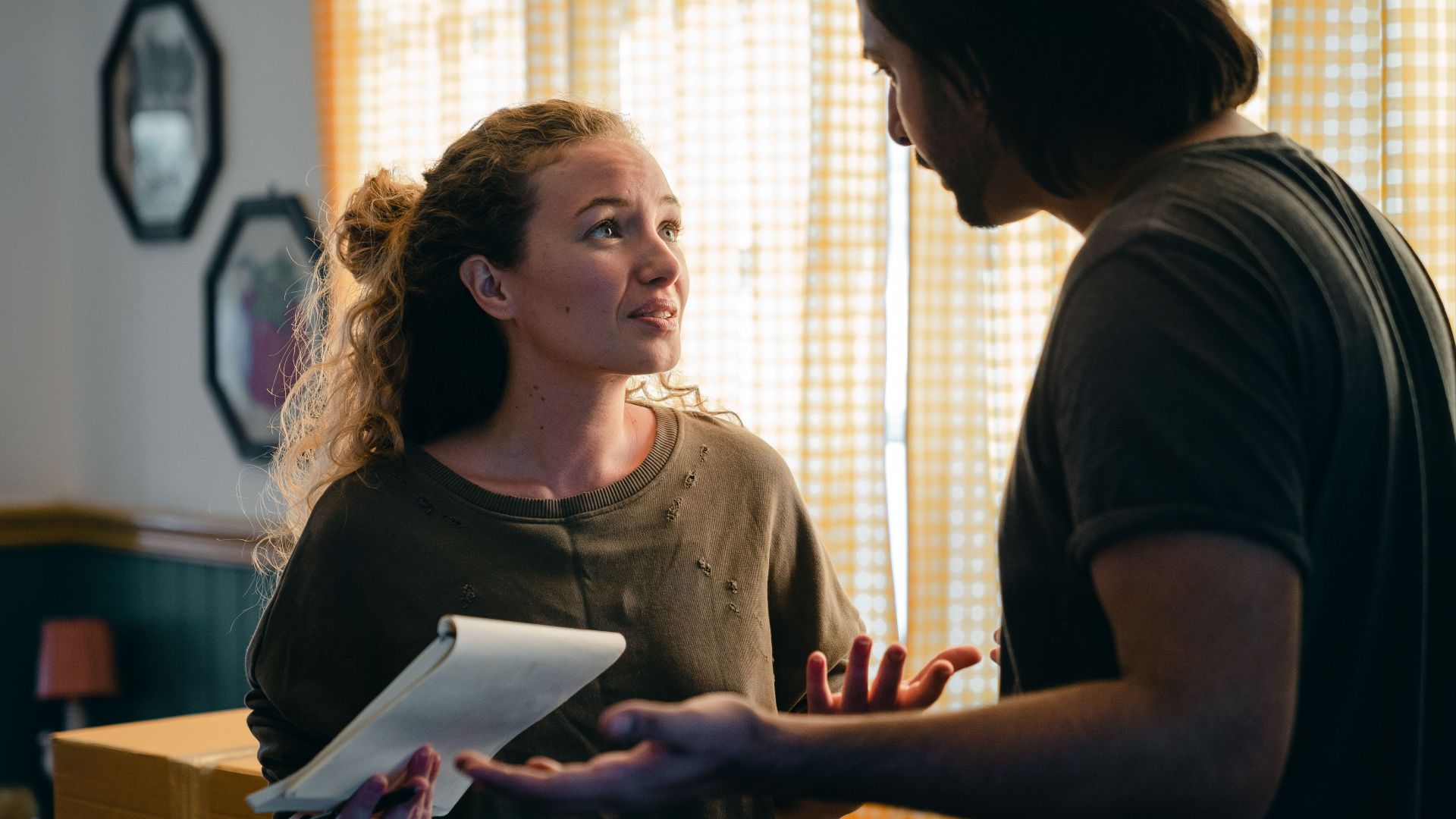 Young perplexed couple wearing casual clothes with notebook looking at each other nervously while unpacking carton box