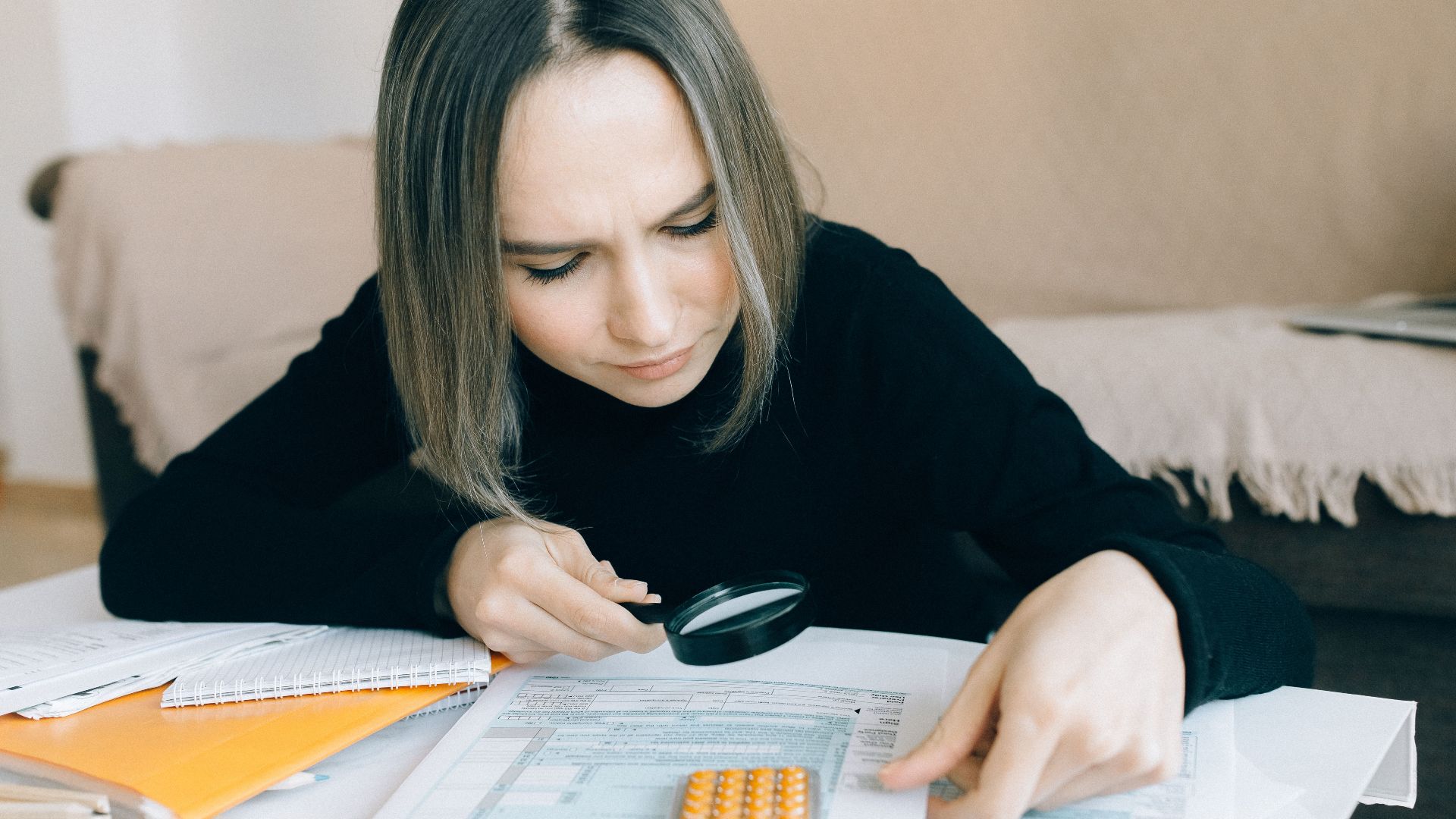 A focused young woman examines documents with a magnifying glass, highlighting attention to detail in accounting tasks.