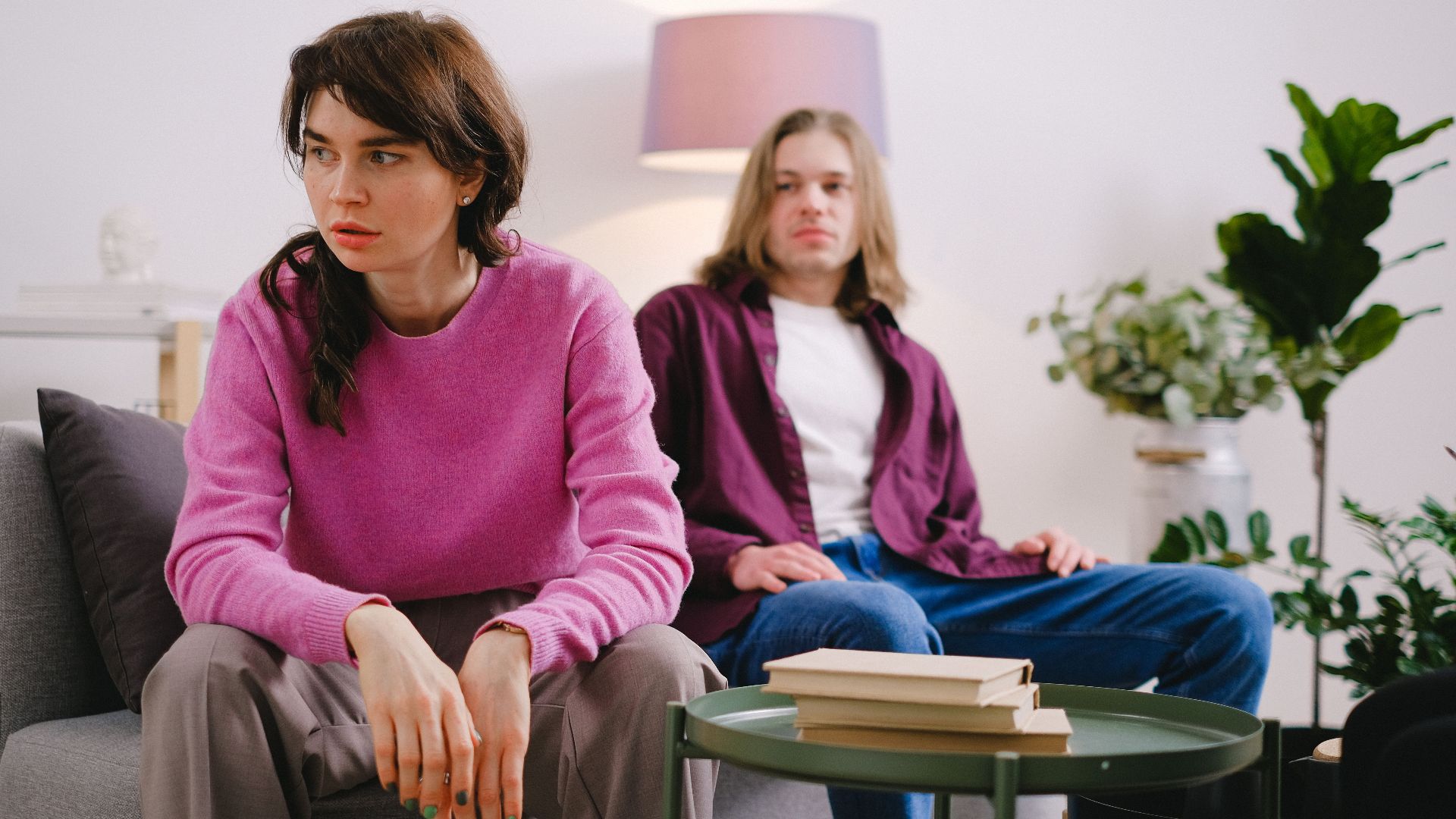 A couple sitting on a sofa with thoughtful expressions, surrounded by home decor.