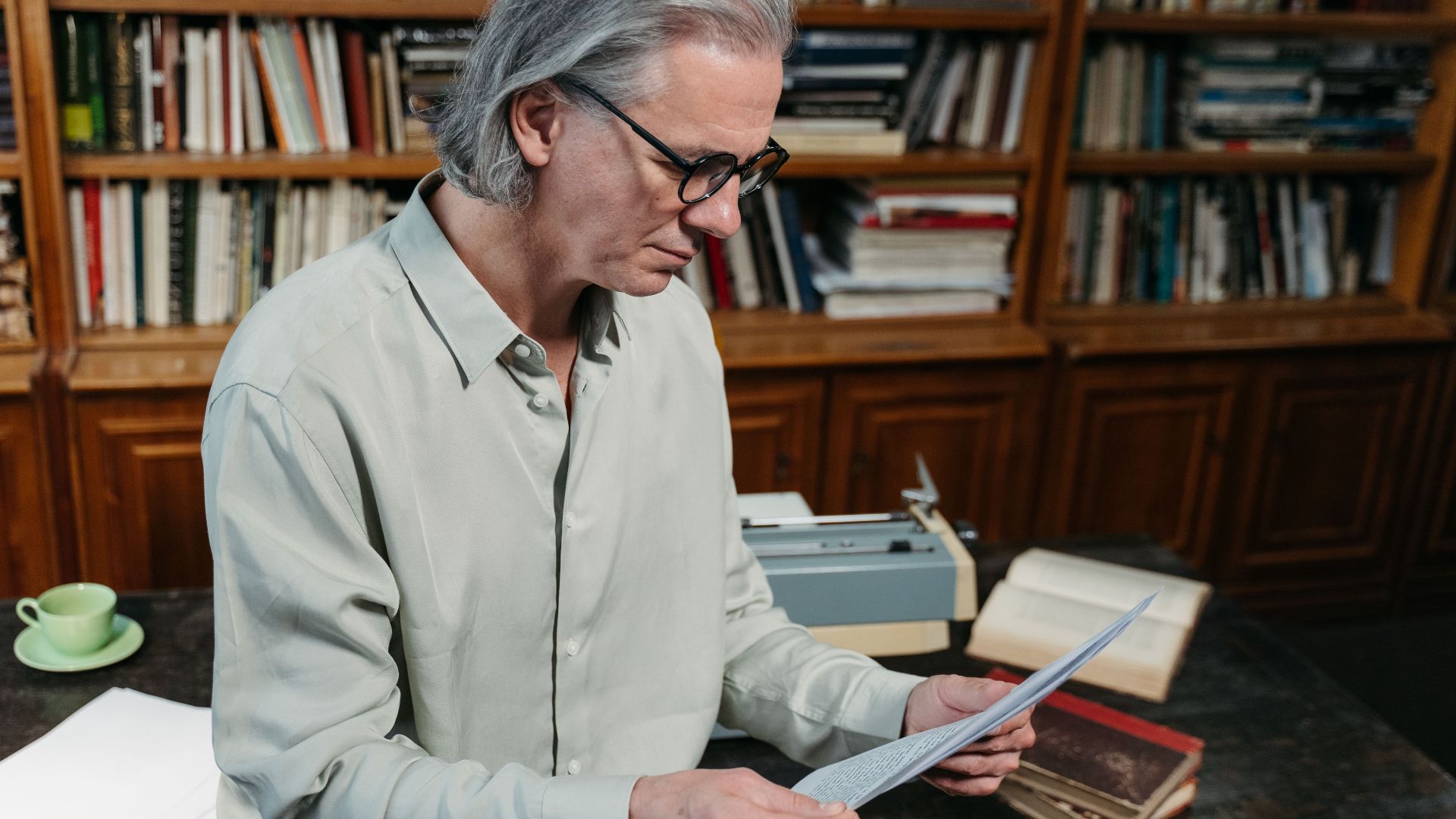 Senior man with gray hair reading documents in a cozy library.