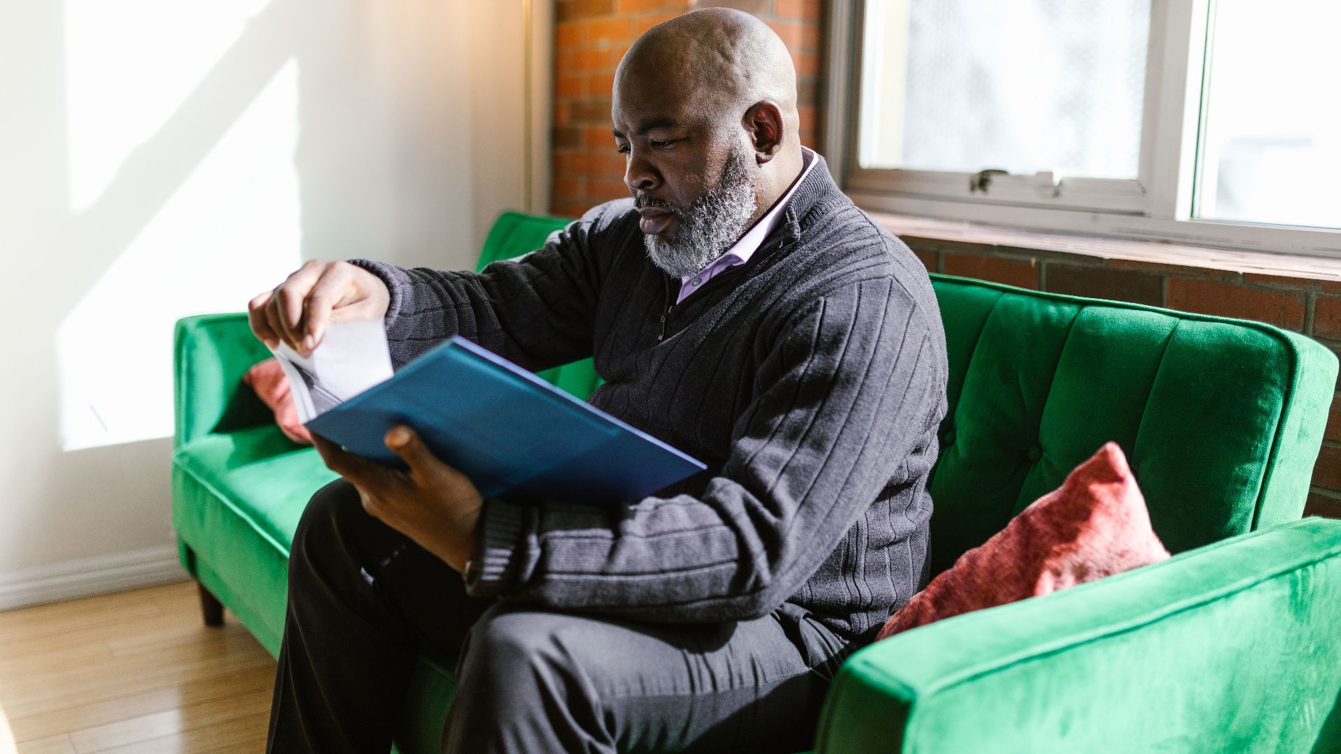An adult man attentively reads papers on a vibrant green sofa in a well-lit room.