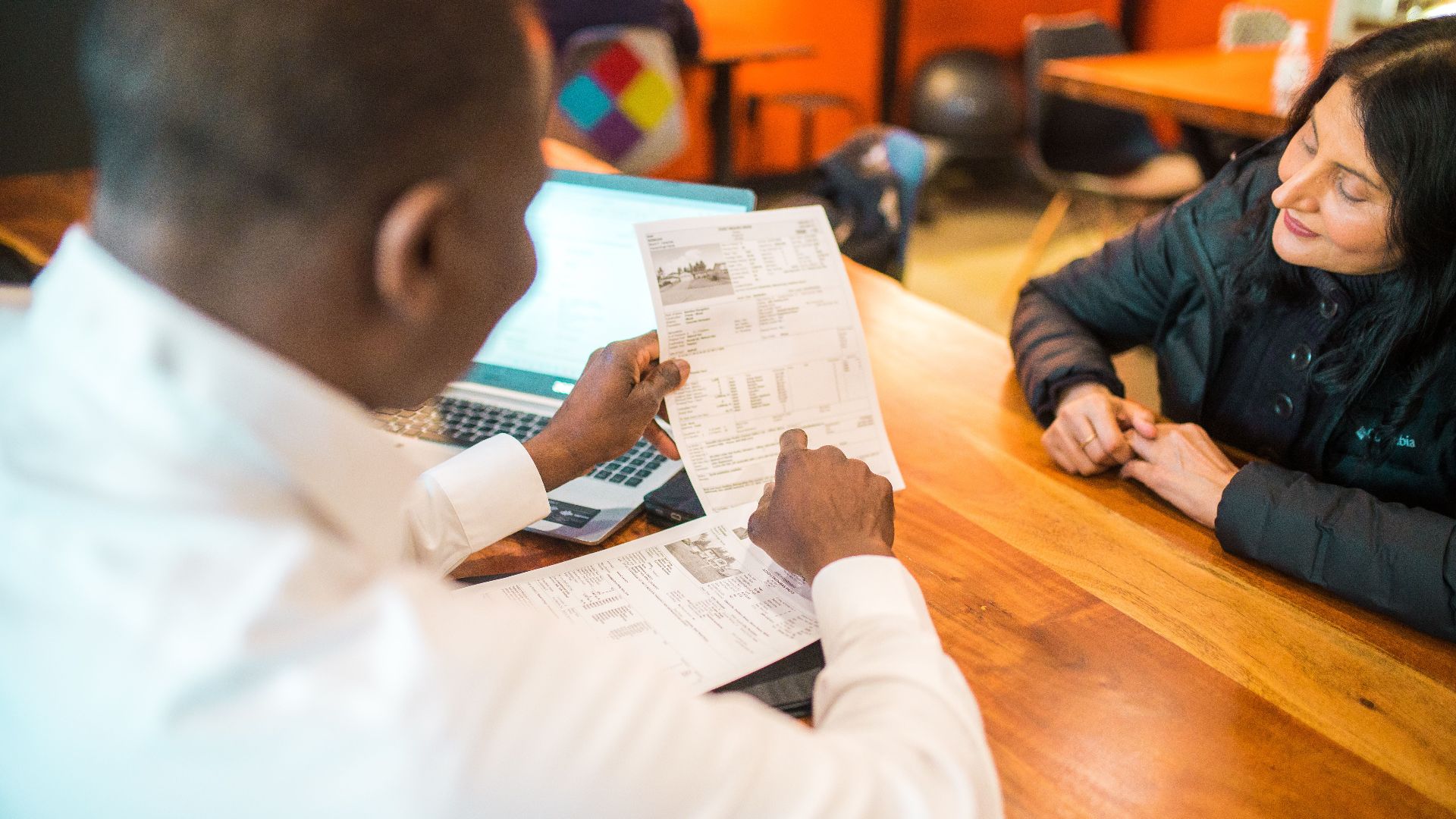 Two adults discussing documents in a business setting indoors.