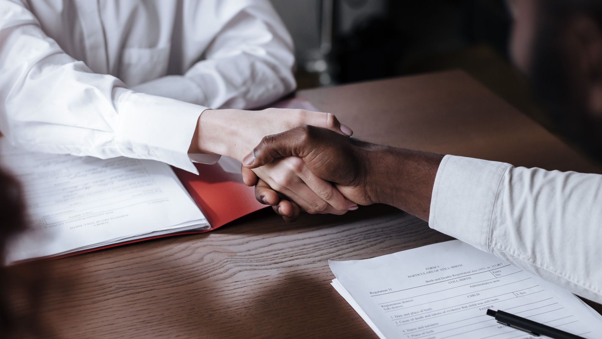 Close-up of a diverse business handshake over documents, symbolizing agreement and collaboration.