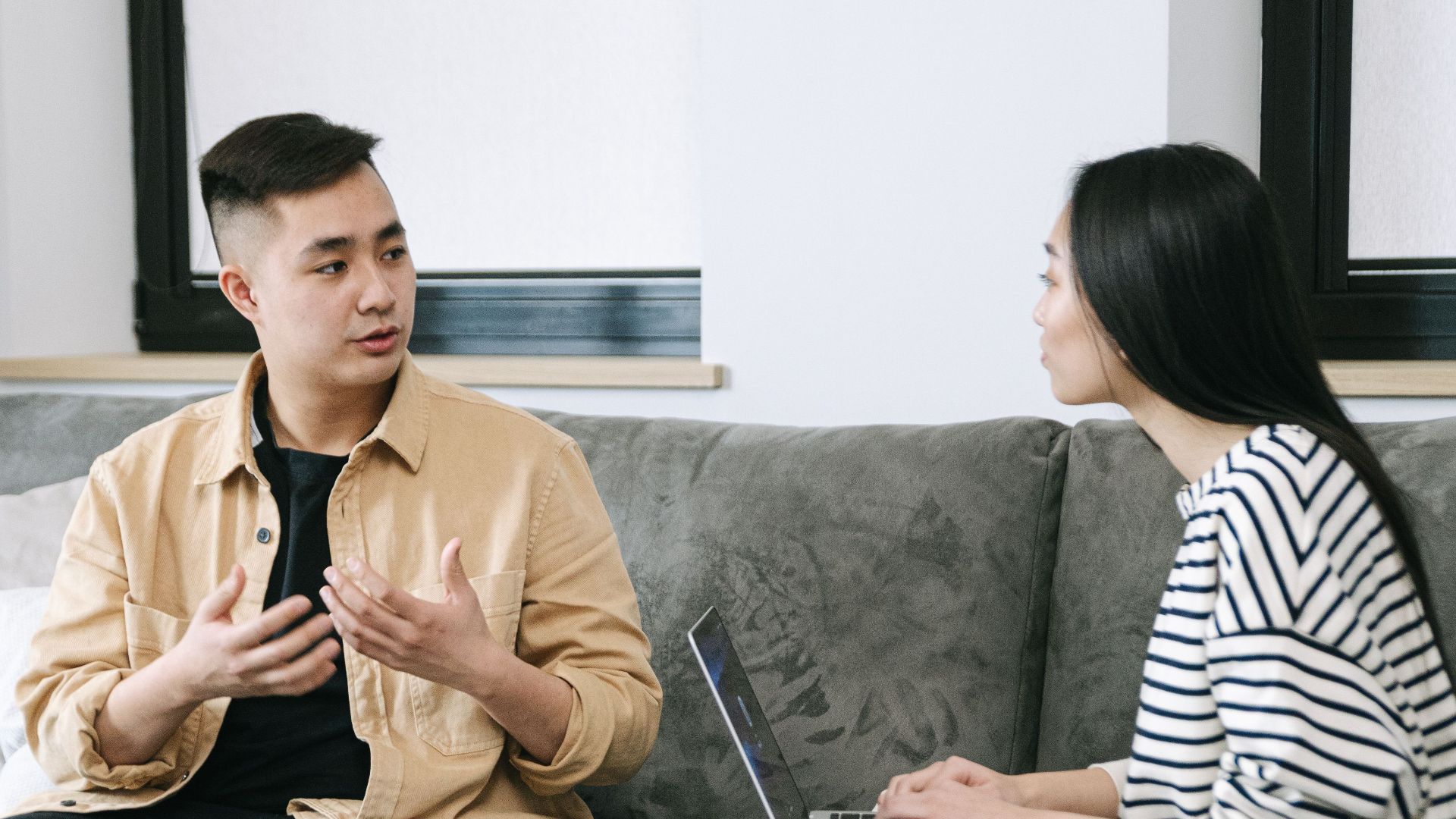 Two young adults engaged in a conversation, sitting on a couch at home.