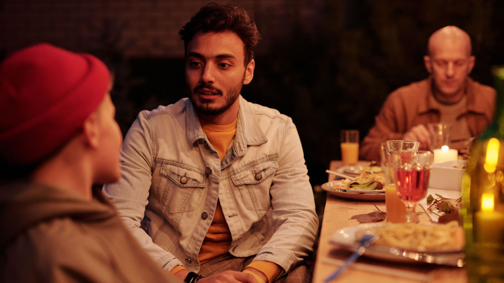 Young Indian man and boy talking at table with dinner and candles enjoying evening with family and friends
