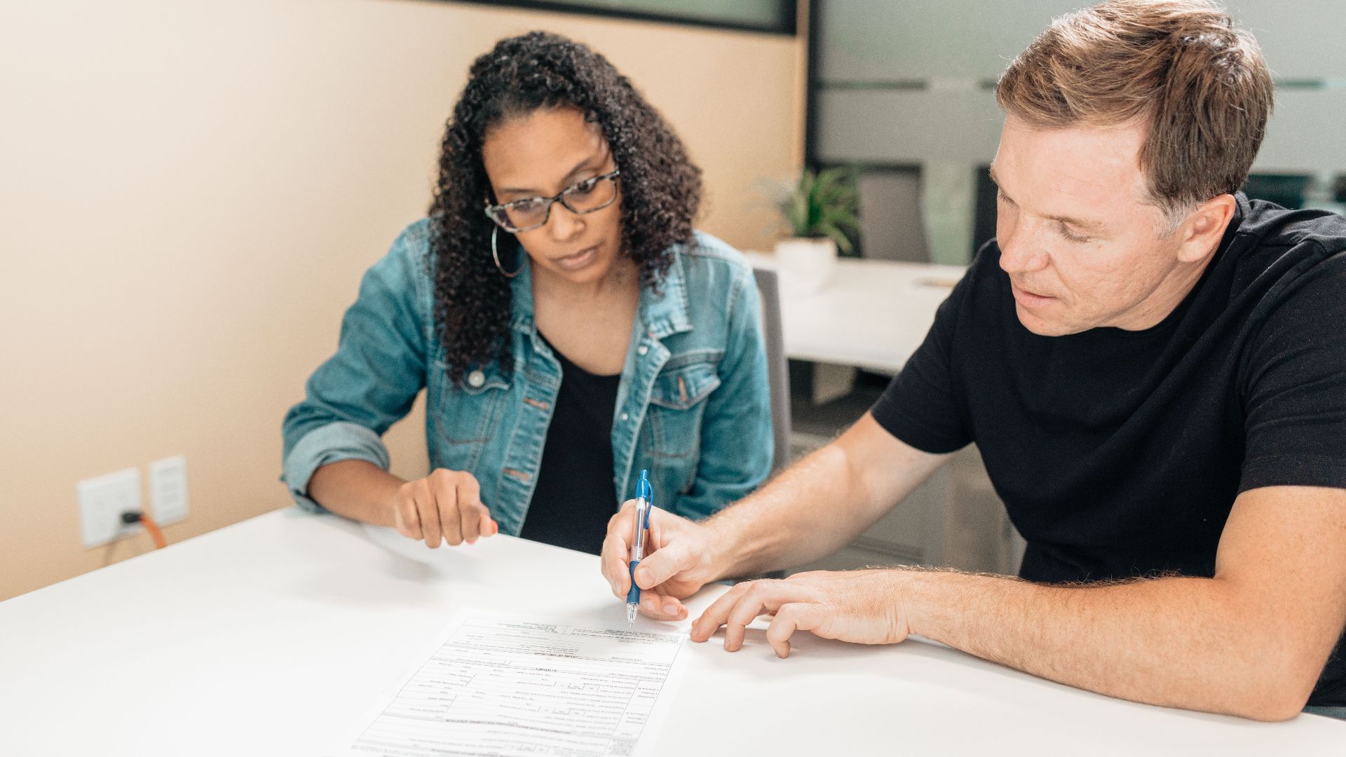 A couple working together to sign important legal documents at a desk in an office setting.