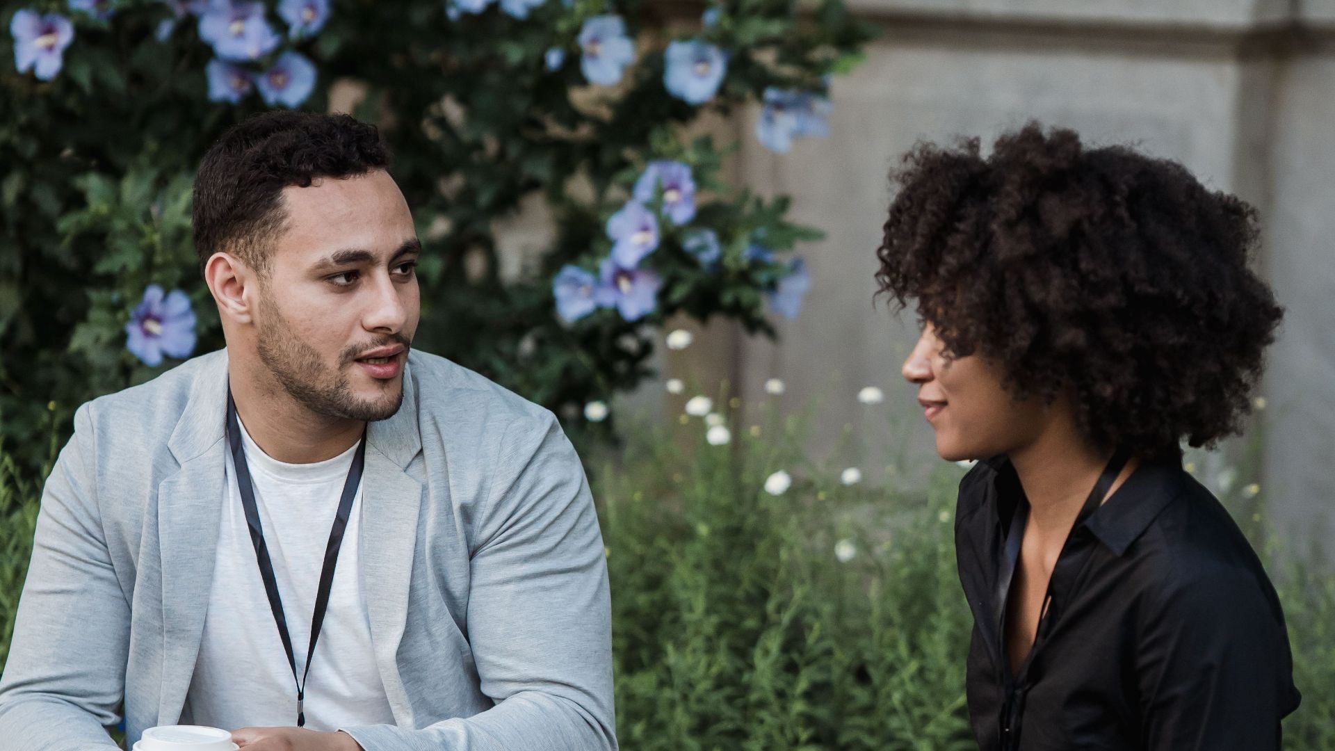 A relaxed couple having a conversation on a park bench surrounded by lush flowers.