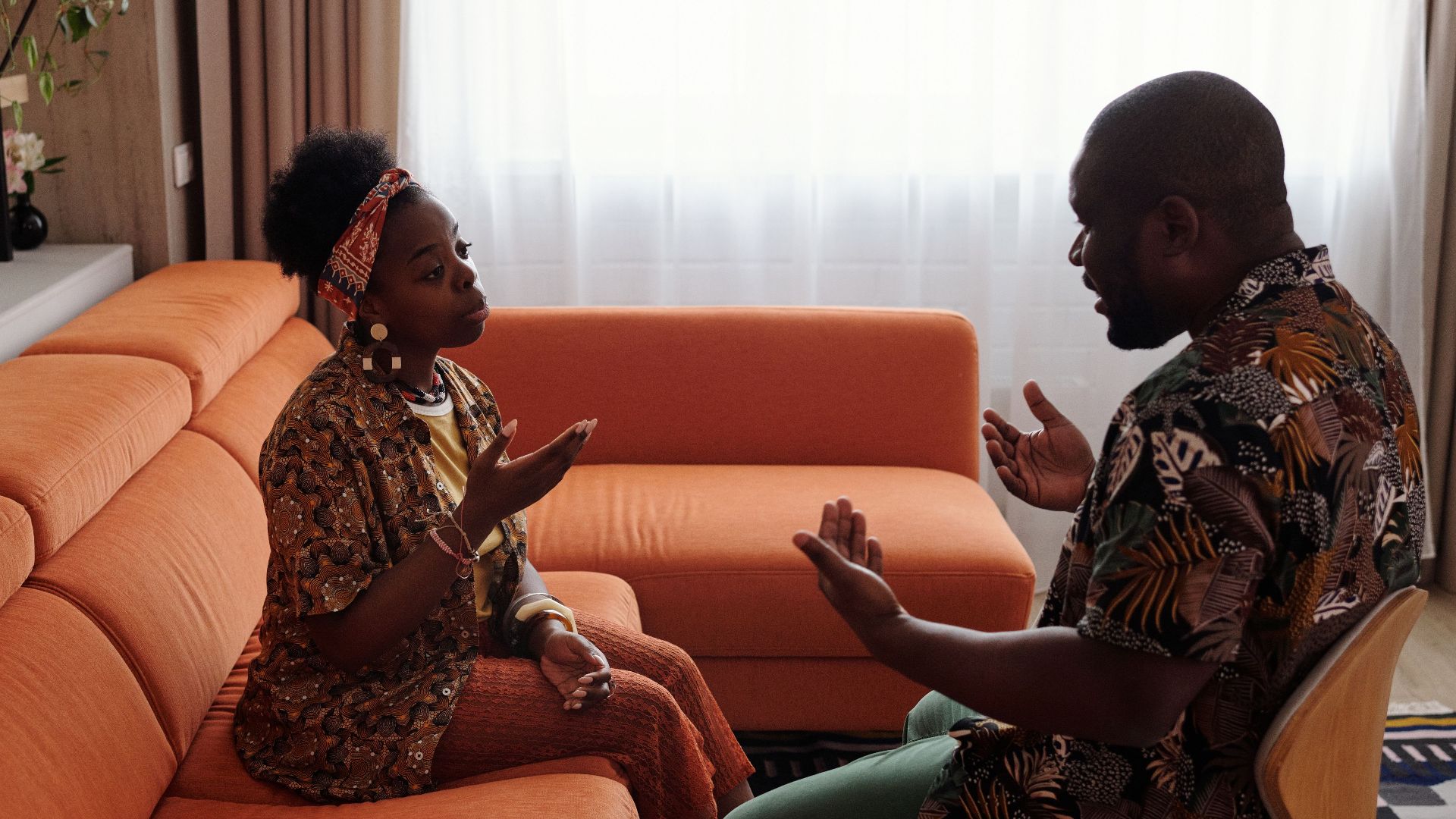A couple having an emotional discussion on an orange sofa in modern living room.