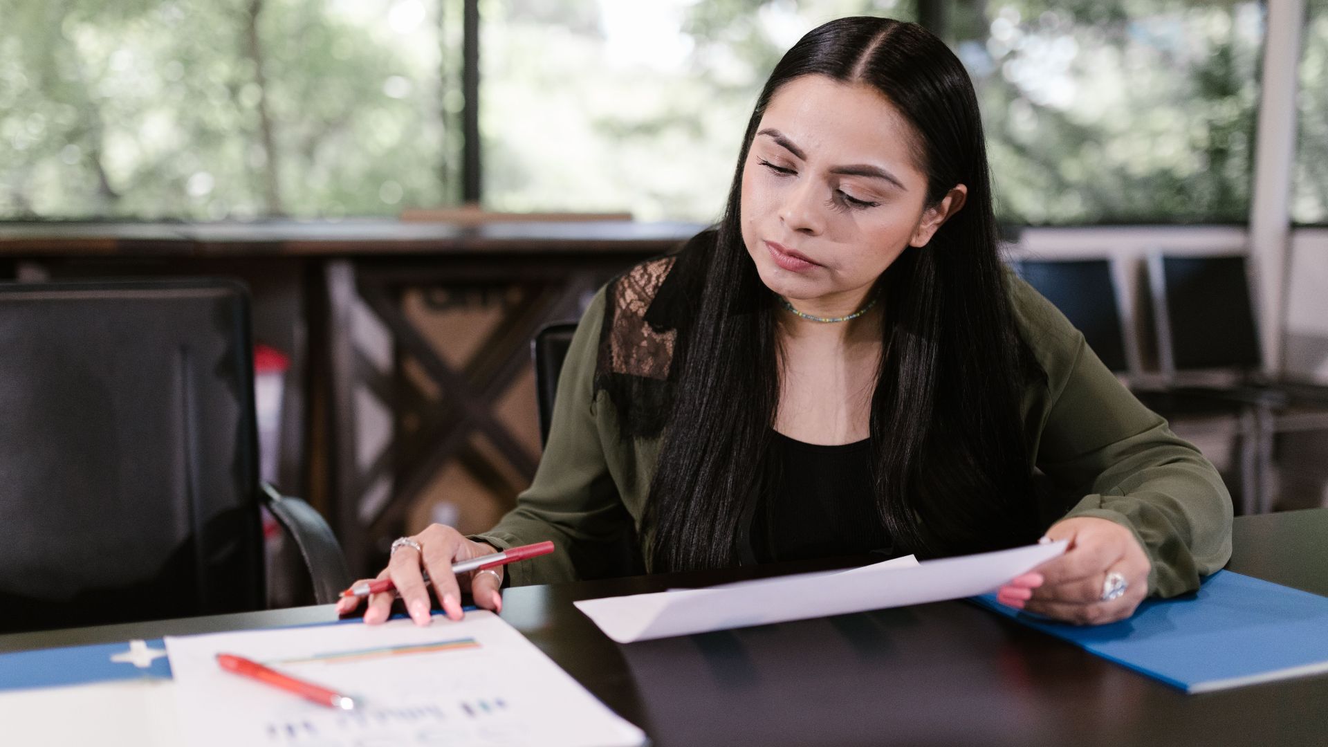 Professional woman in office setting studying documents with concentration.