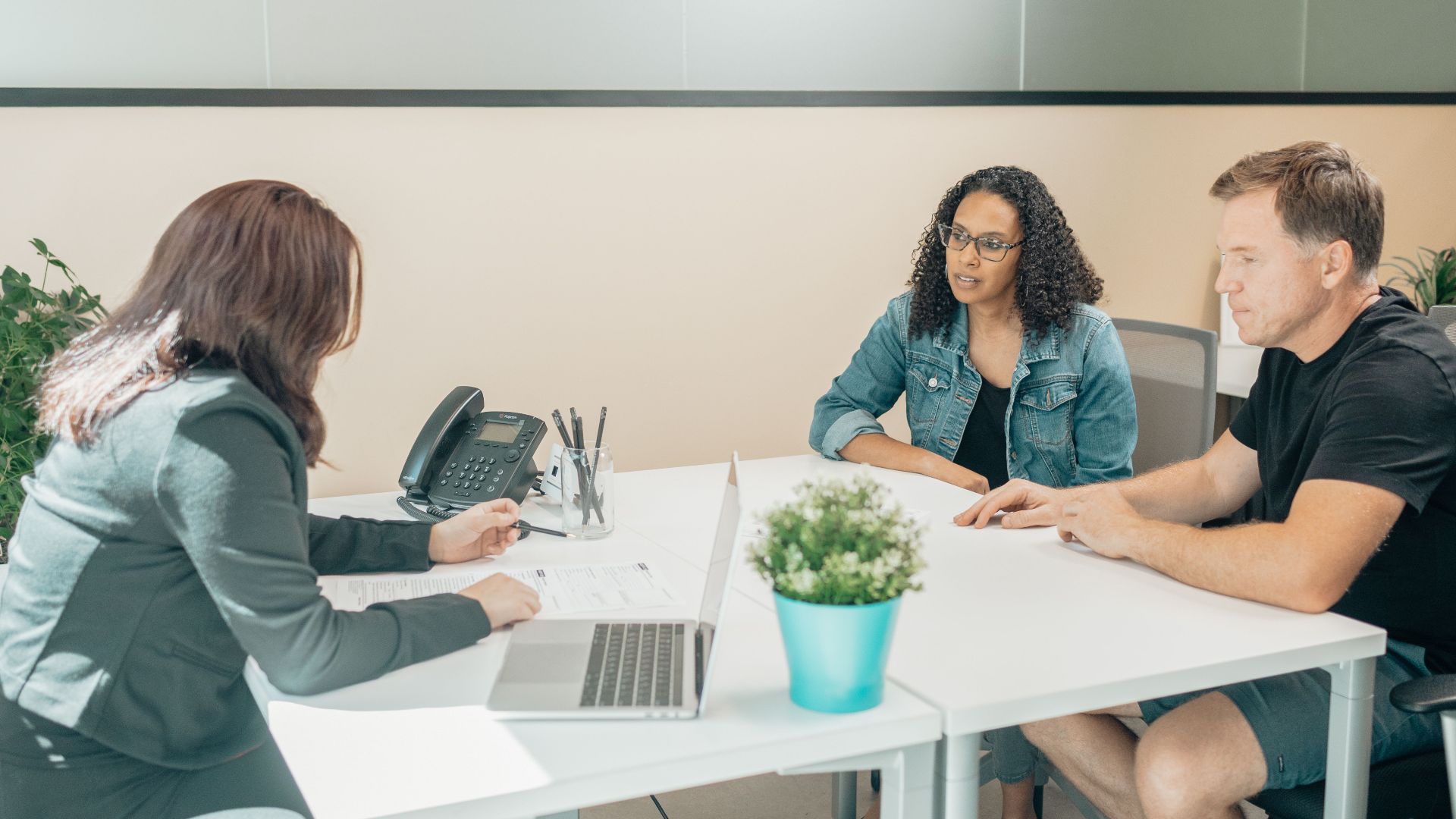 Anonymous female employee interacting with diverse clients at table with netbook and paper sheet in workspace