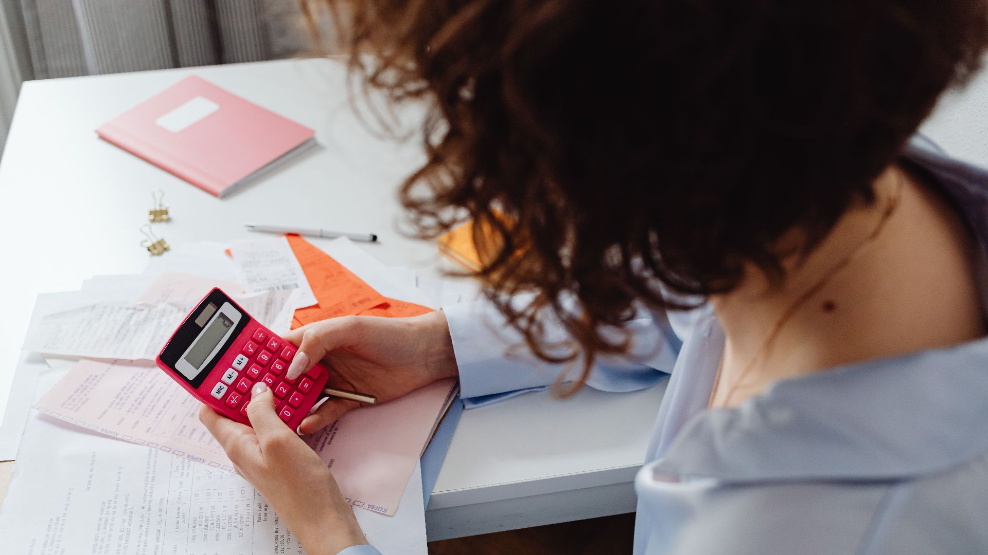 Woman calculating expenses with documents and calculator at work desk.