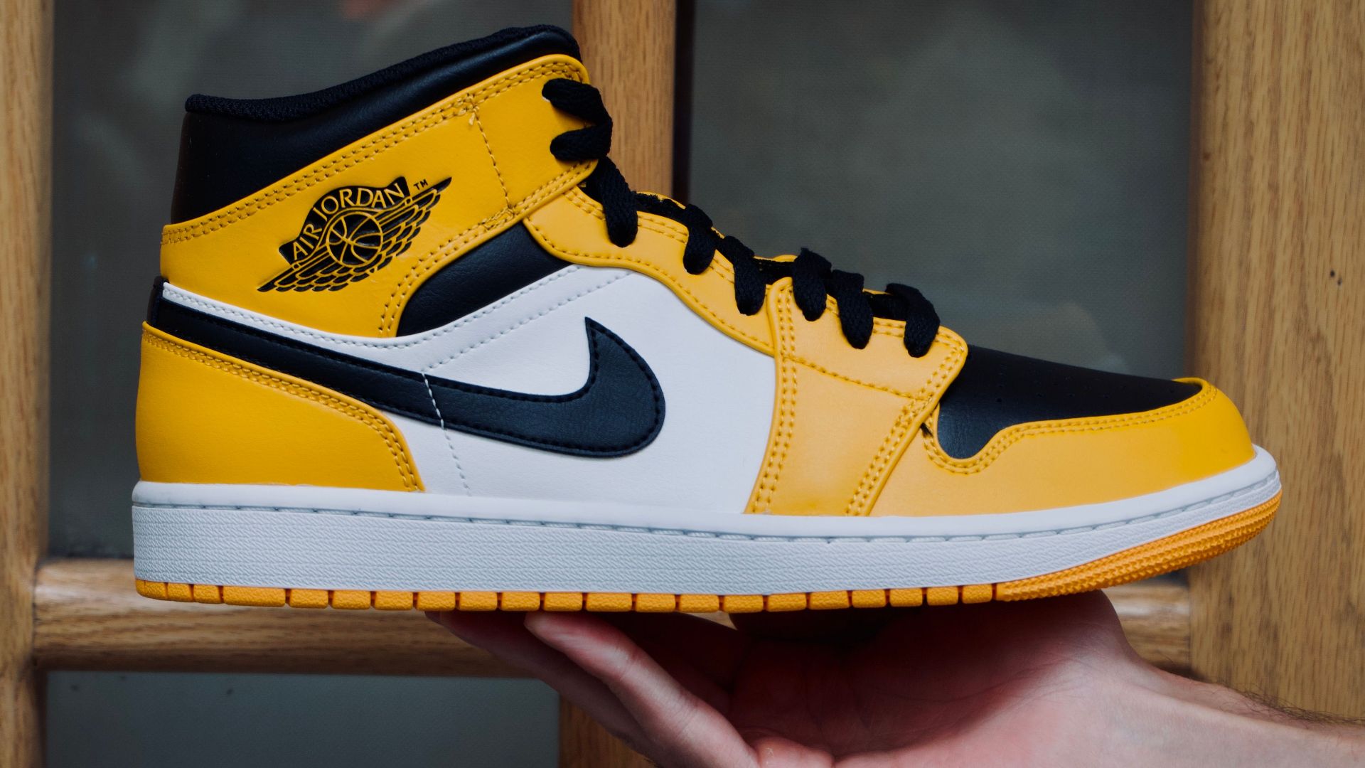 Close-up of a yellow and black sneaker being held in front of a wooden door. Modern fashion footwear.