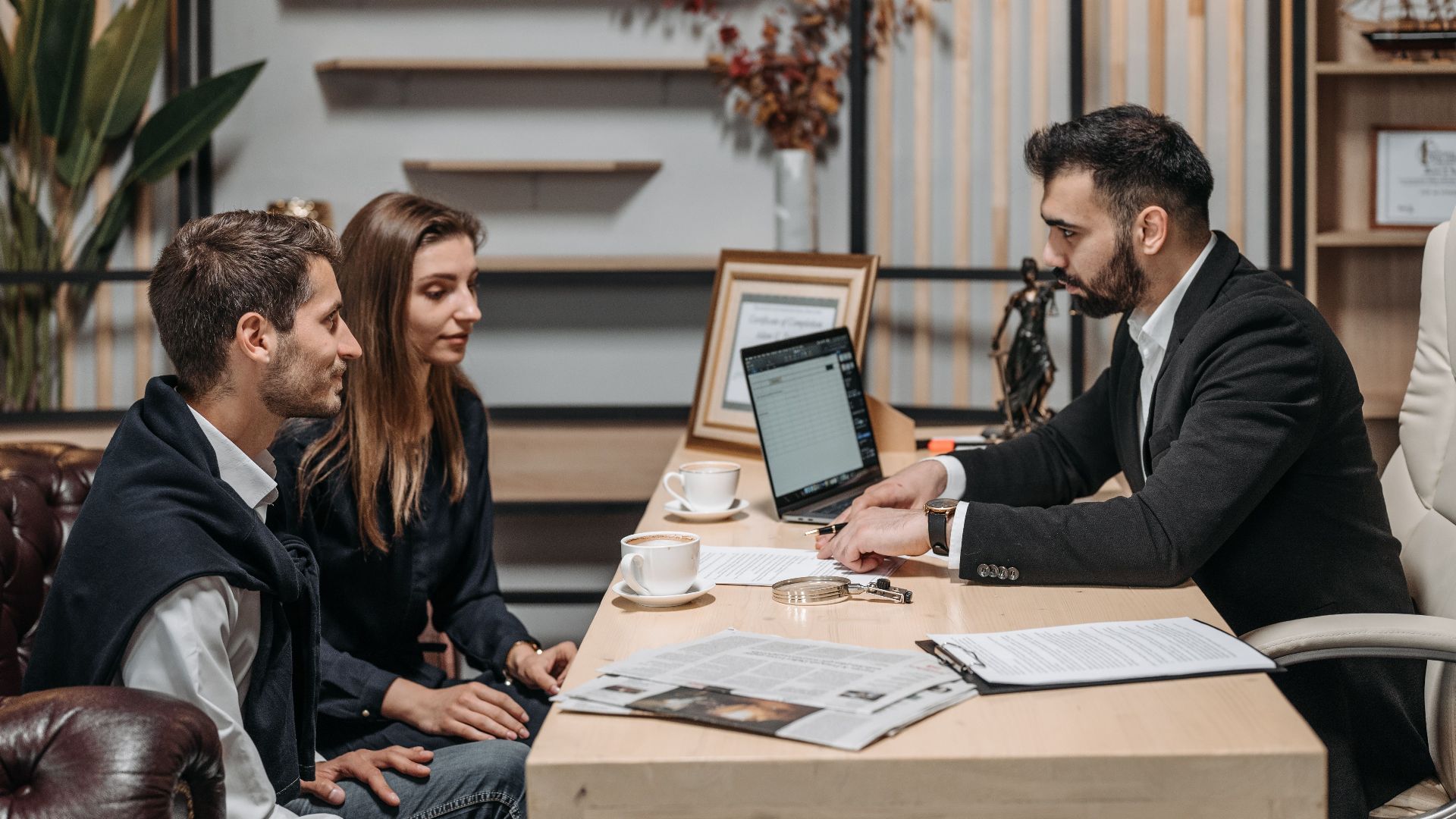 Three professionals engaged in a business discussion at an office desk with a laptop.