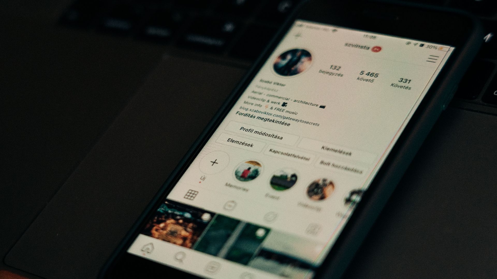 Close-up of smartphone showing a social media profile screen next to a laptop.
