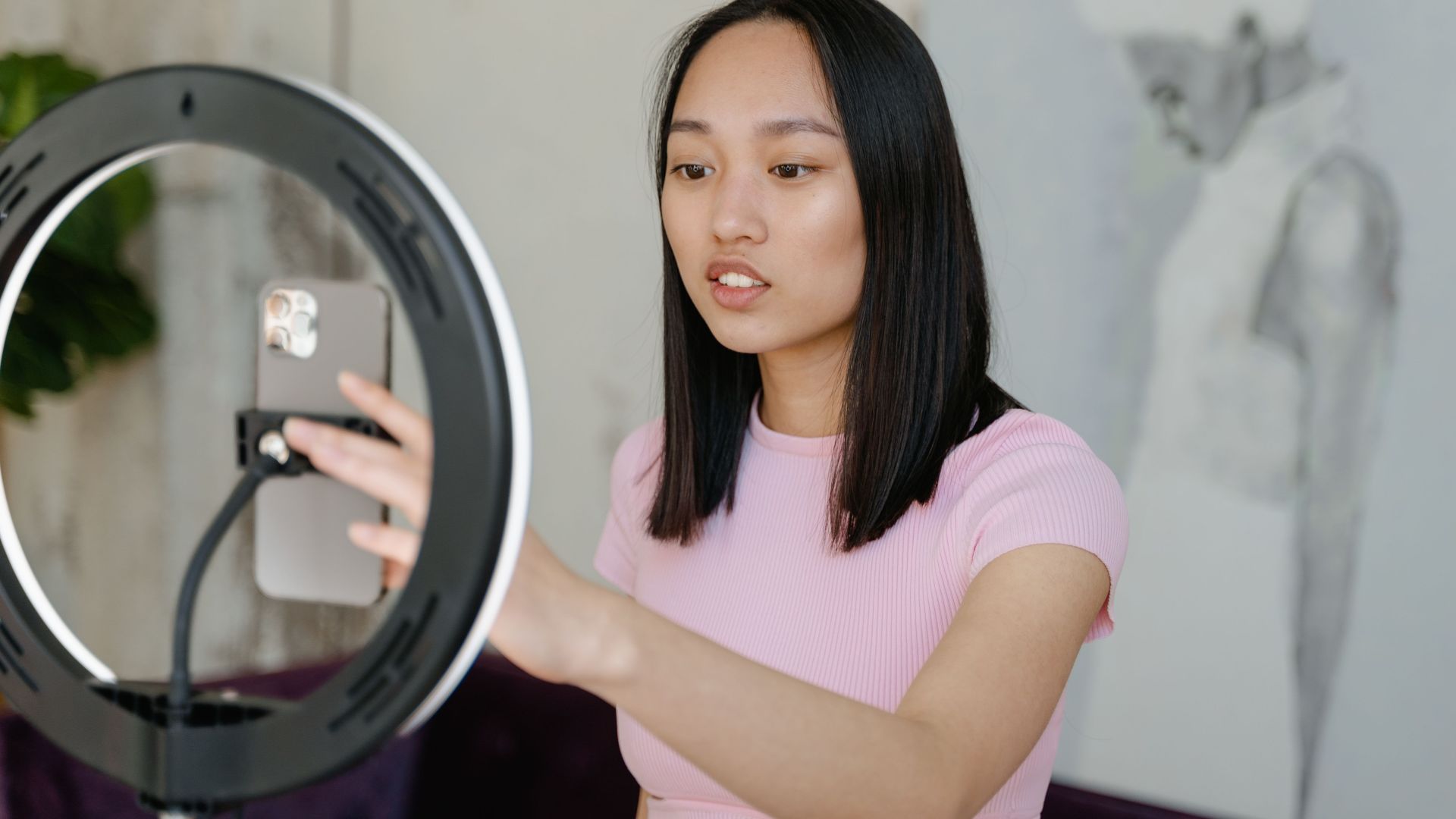 Young woman using a smartphone and ring light for social media content indoors.