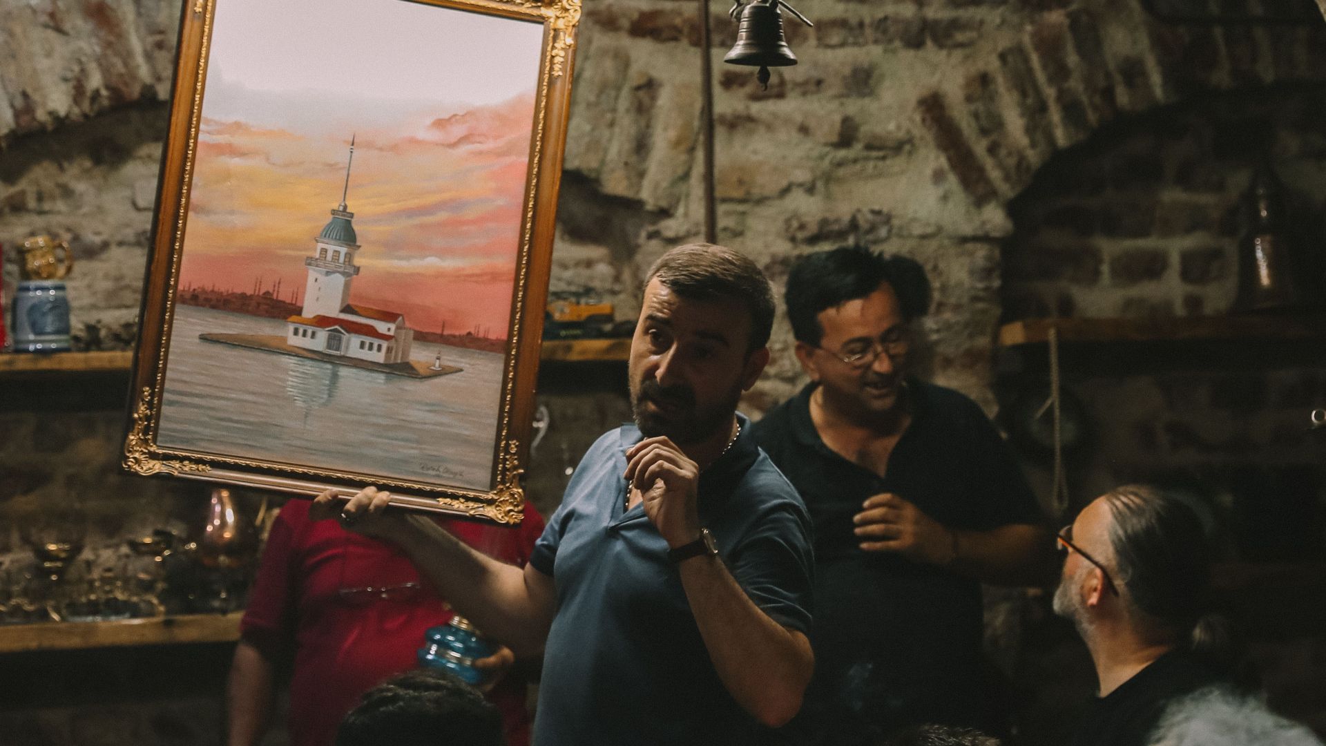 Art auction with painting of Istanbul's Maiden's Tower held in a historic indoor venue.