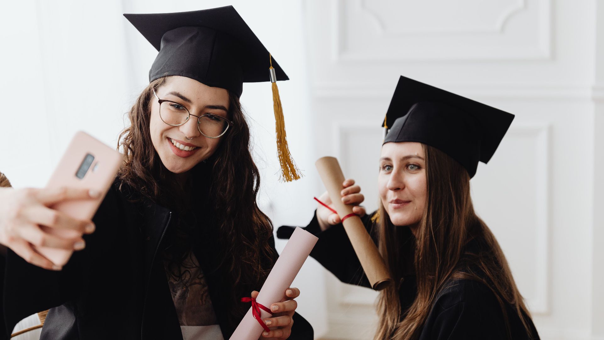 Cheerful young women in graduation caps taking a selfie during a joyful celebration.