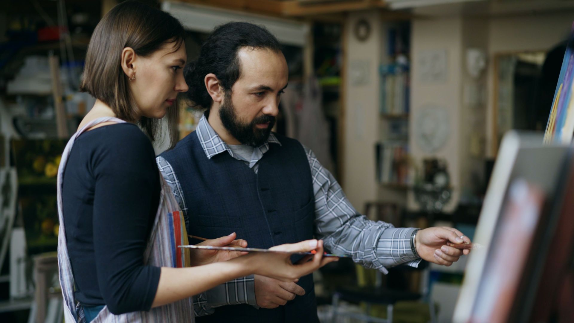 Two artists collaborating in an indoor studio, focused on painting and creativity.