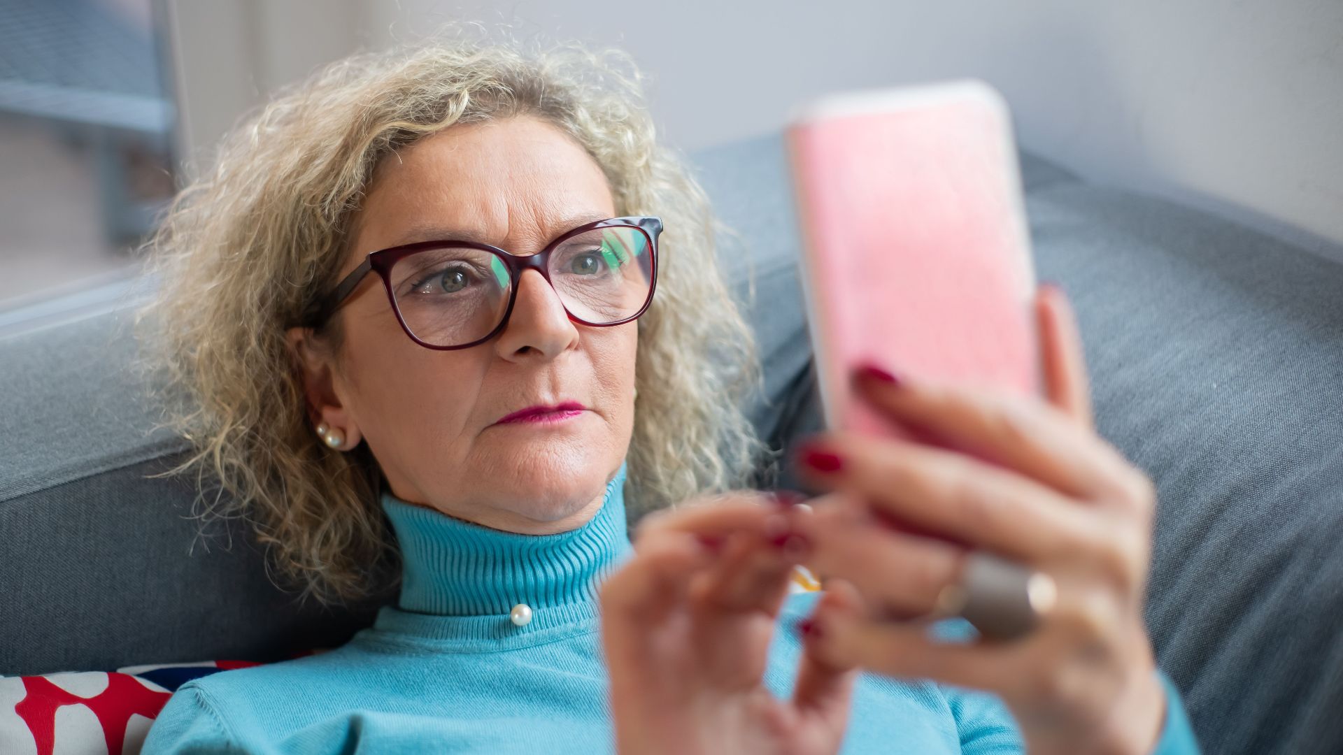 Elderly woman in glasses using smartphone indoors, focused on screen.