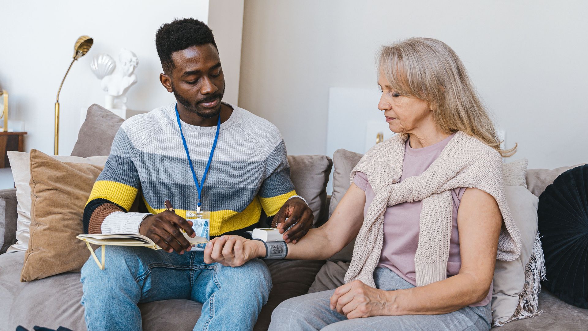 Volunteer checking elderly woman's blood pressure at home. Compassionate healthcare support.