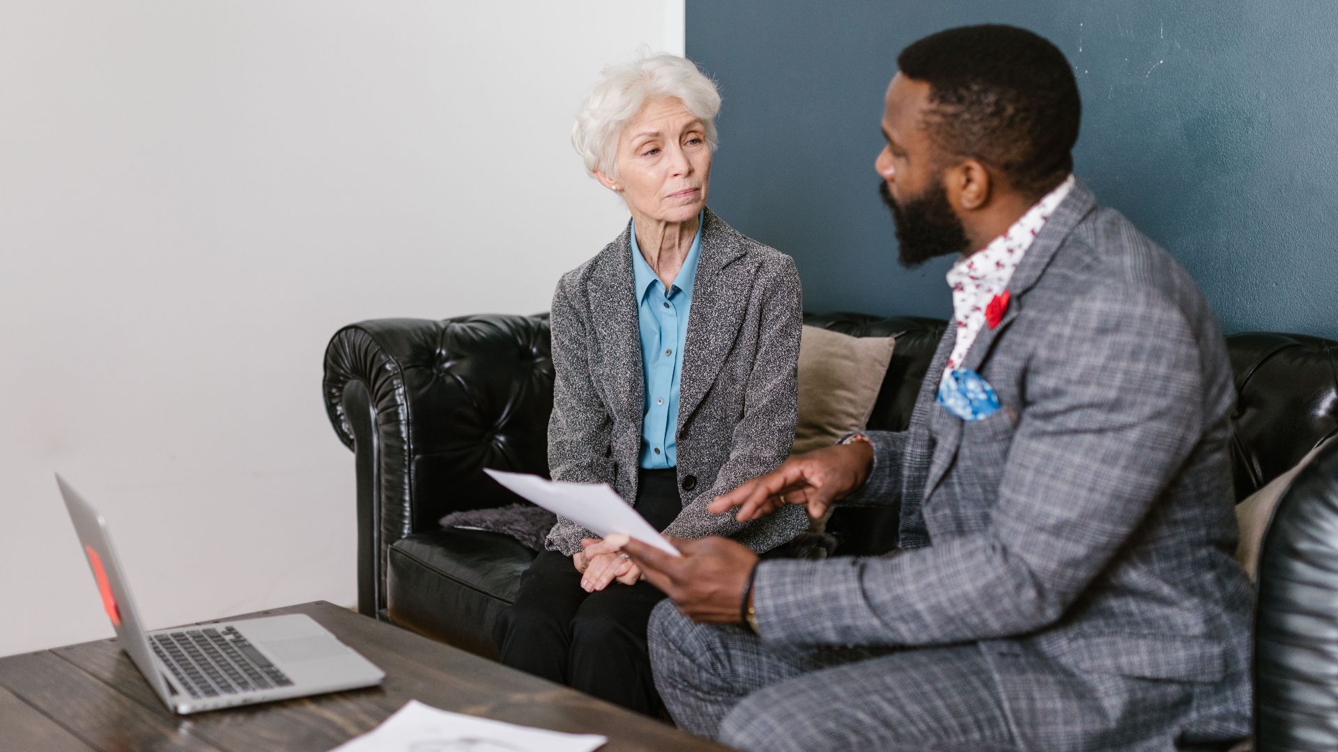 An elderly woman and a man in a professional meeting discussing documents indoors.
