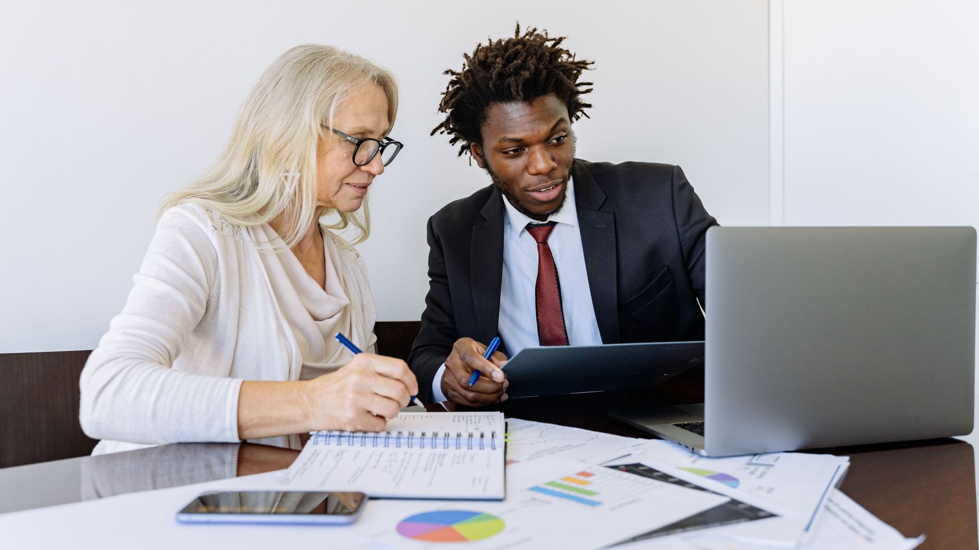Two business professionals collaborating at a desk with laptops and documents in an office setting.