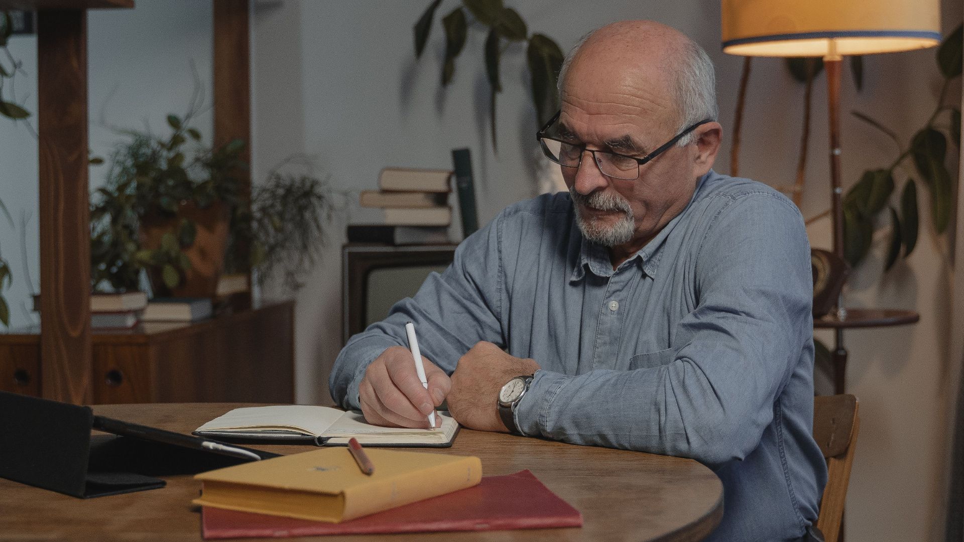 Elderly man pens thoughtful entries in his journal while sitting at a cozy home table.
