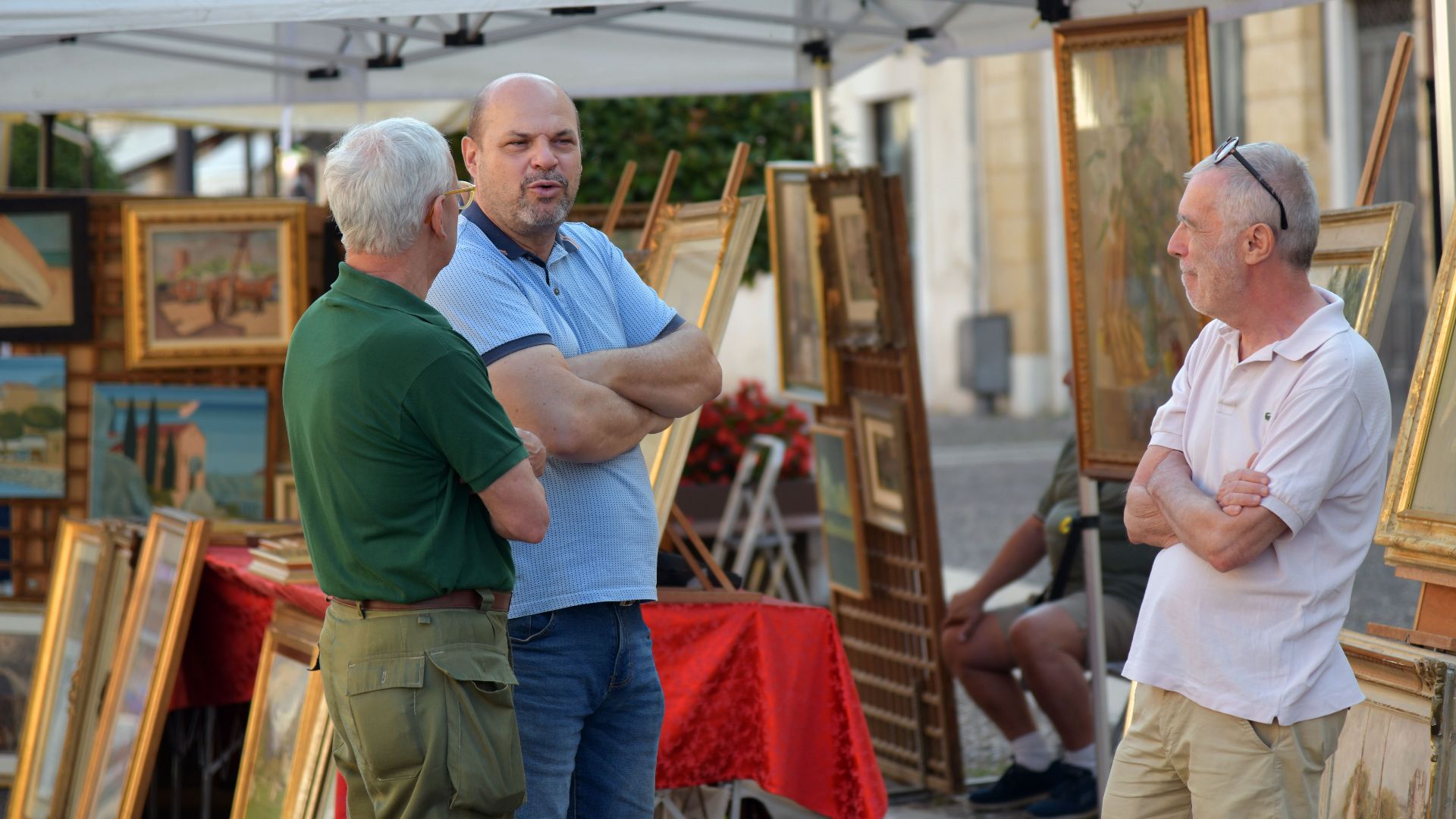 Three men conversing at an outdoor art market in Villafranca di Verona, Italy.