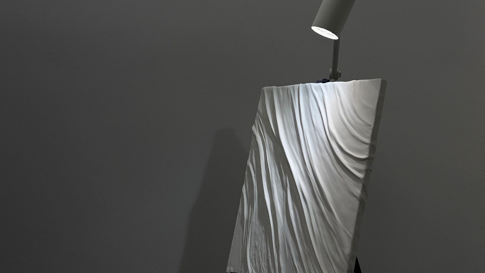 A minimalist abstract art piece on an easel illuminated by a spotlight, creating a dramatic effect.