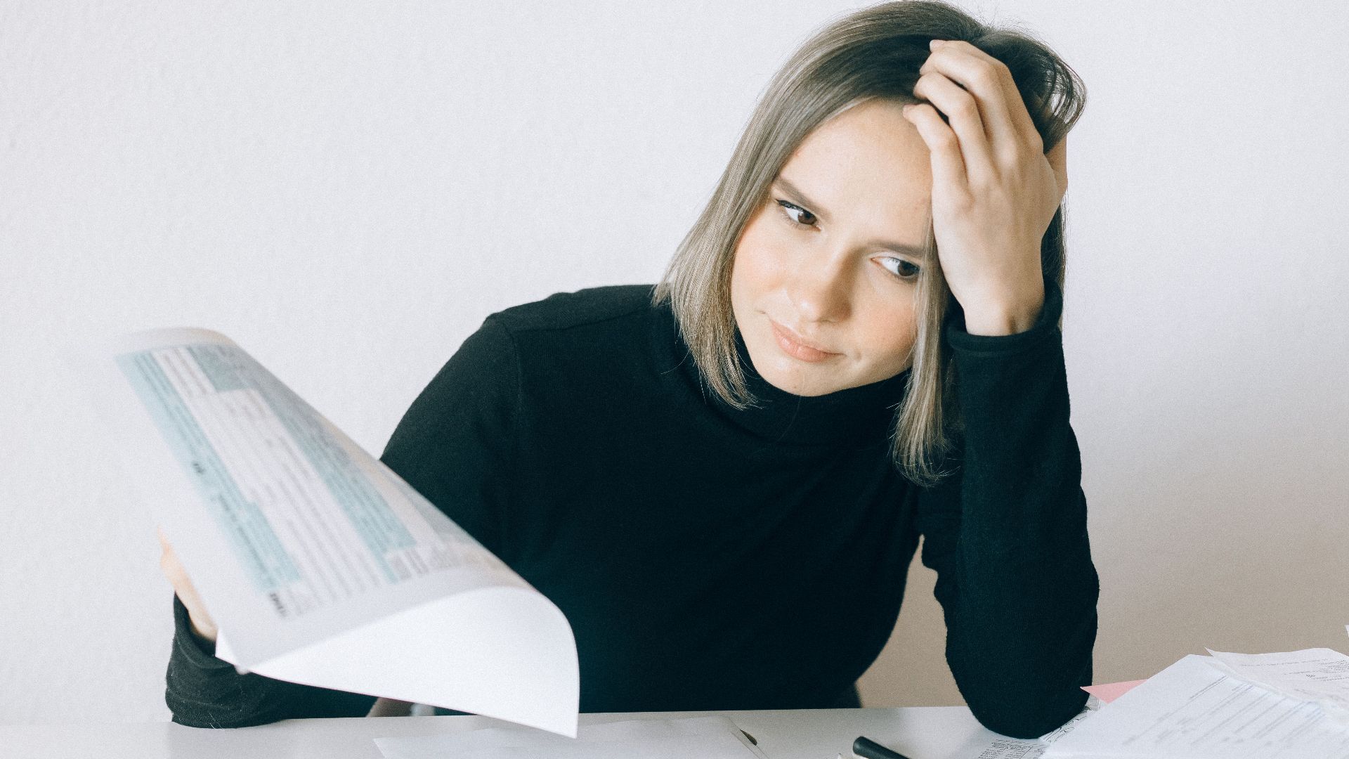 A woman showing stress while reviewing multiple paperwork and financial documents at a desk.