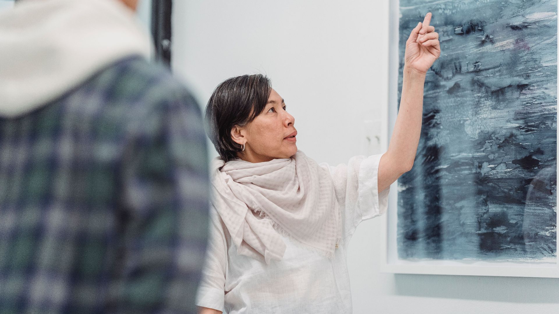 Woman presenting abstract painting in an art gallery setting, engaging discussion.