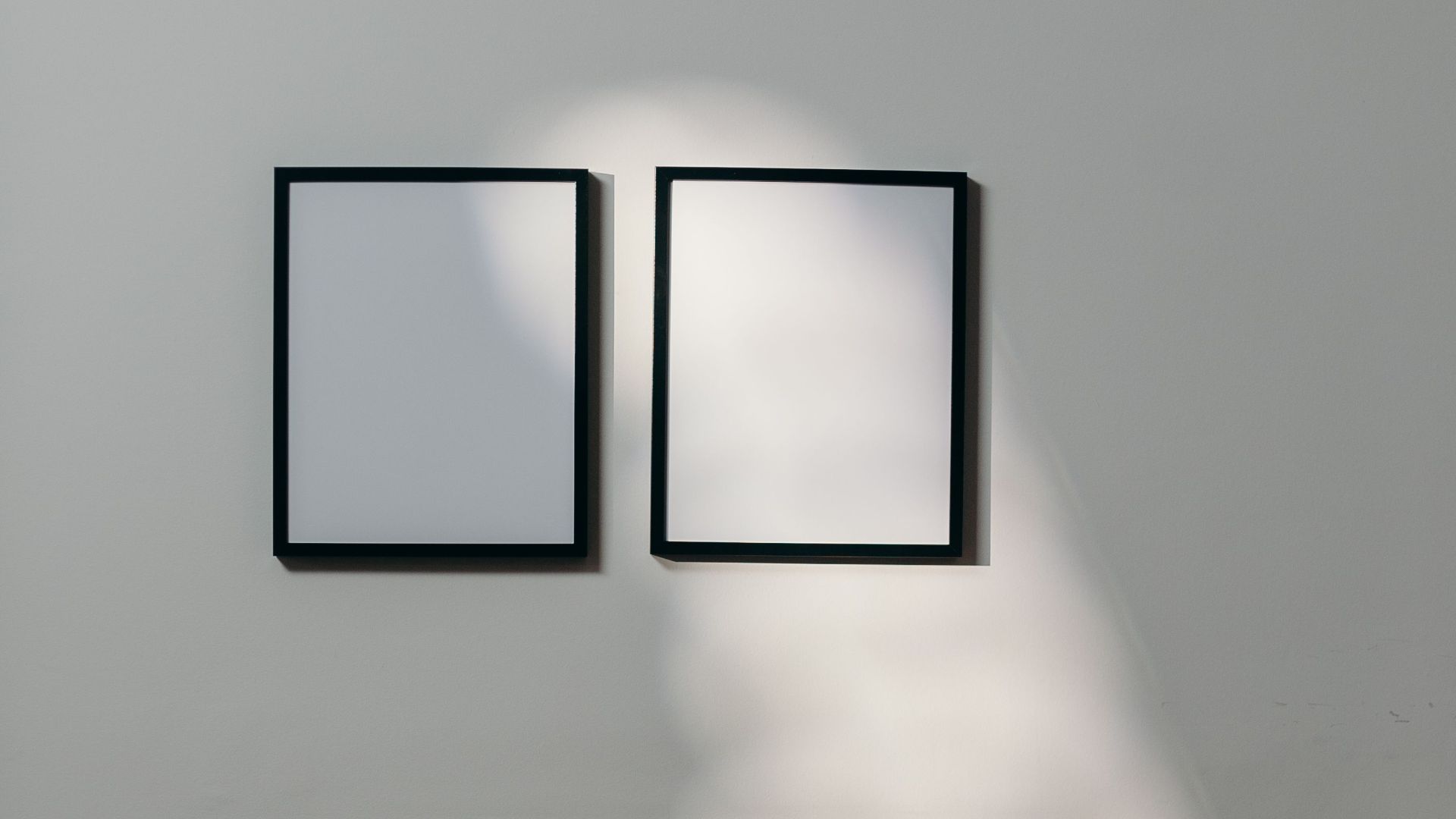 Stylish minimalist interior with black chair and blank frames casting shadows.