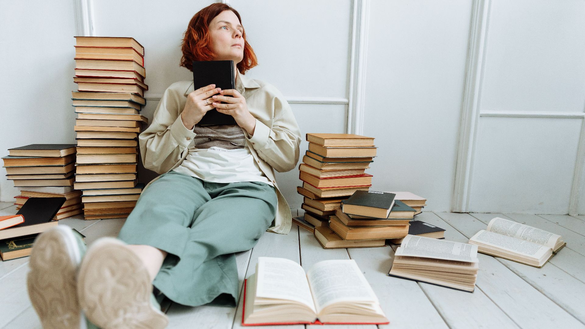 Contemplative woman sitting with books, reflecting in an indoor setting.